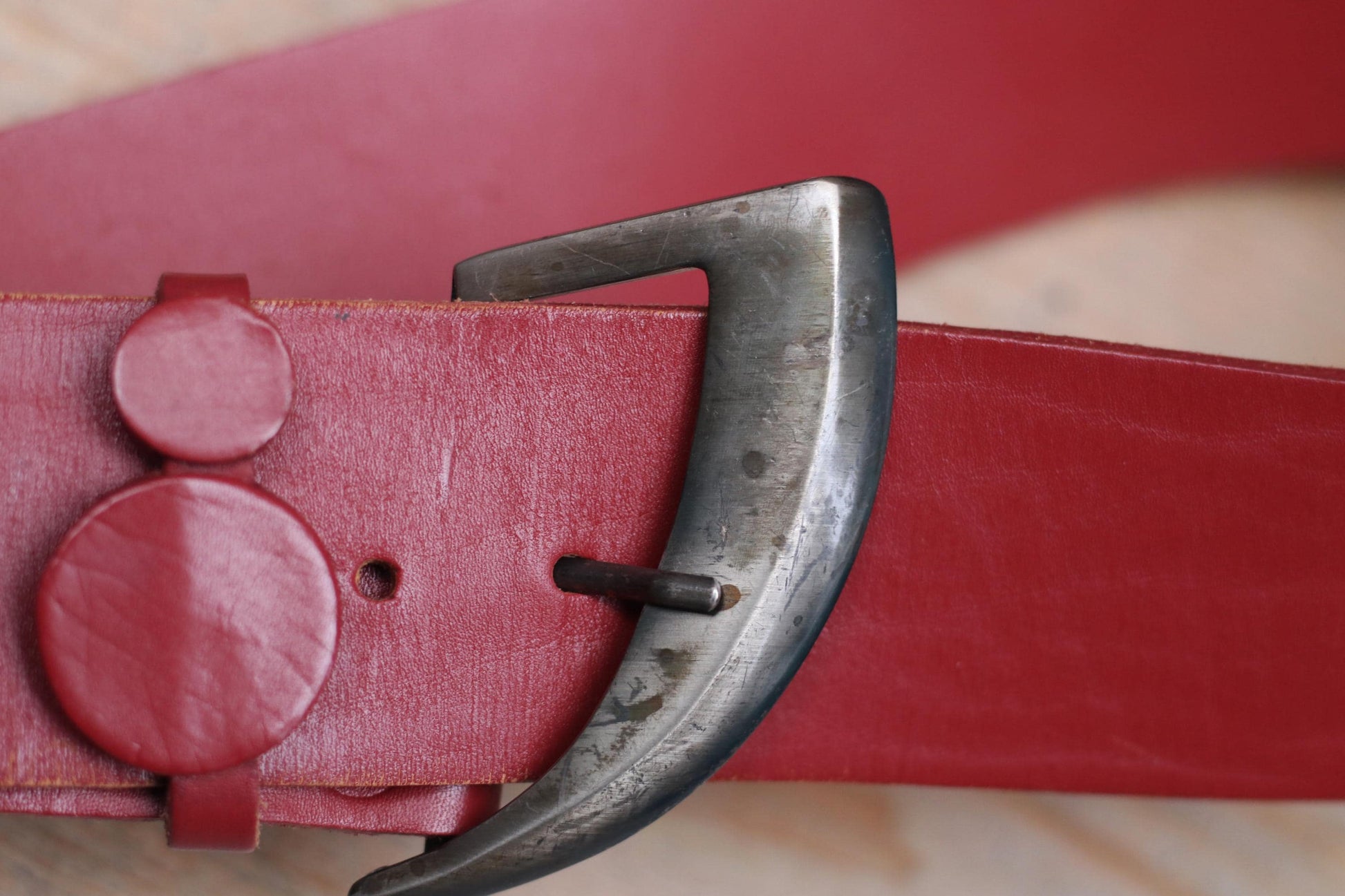 Close-up of a stylish vintage red leather belt with a metal buckle on a wooden surface.