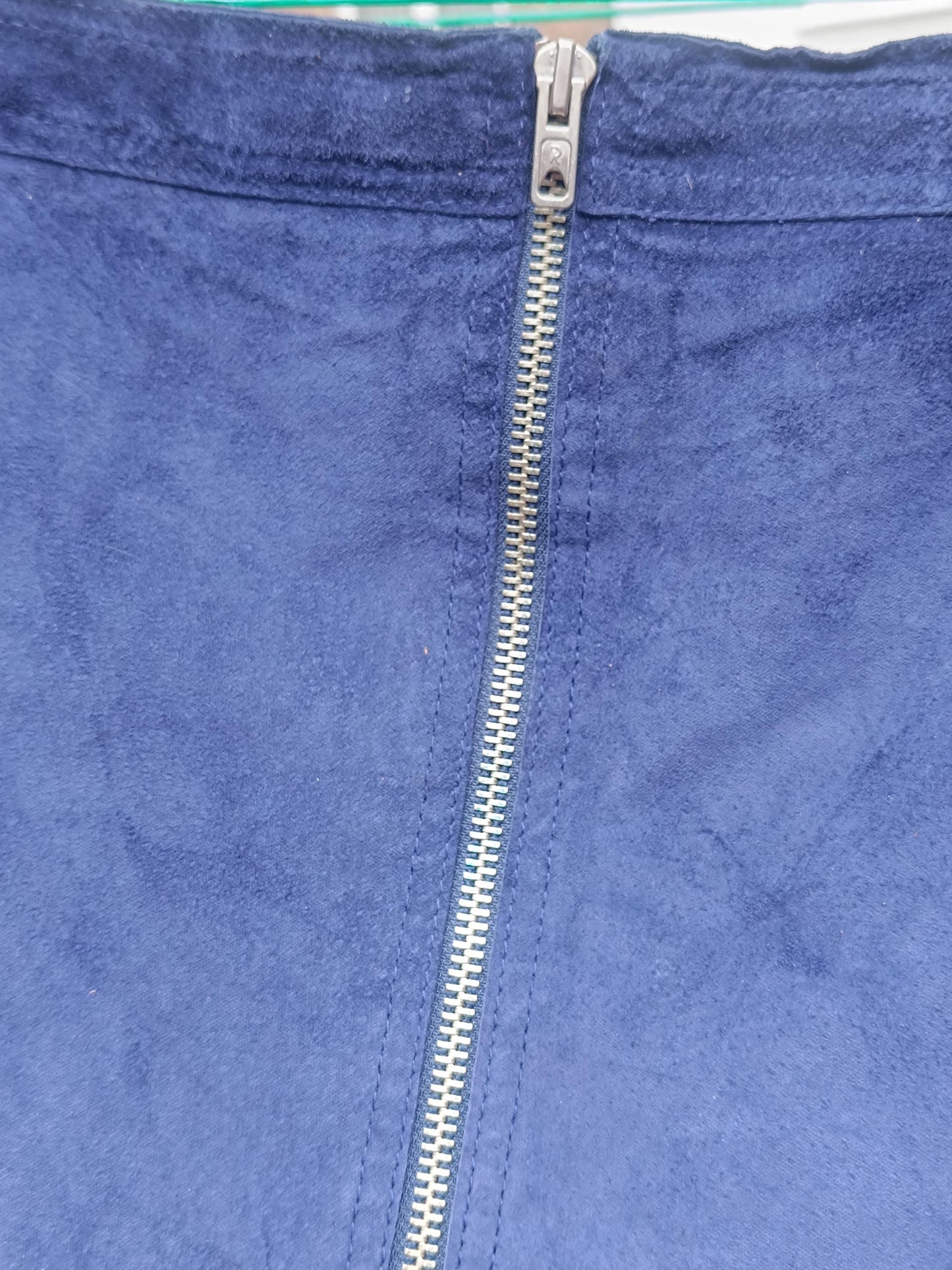 A close-up of a blue suede skirt with a silver zipper in front