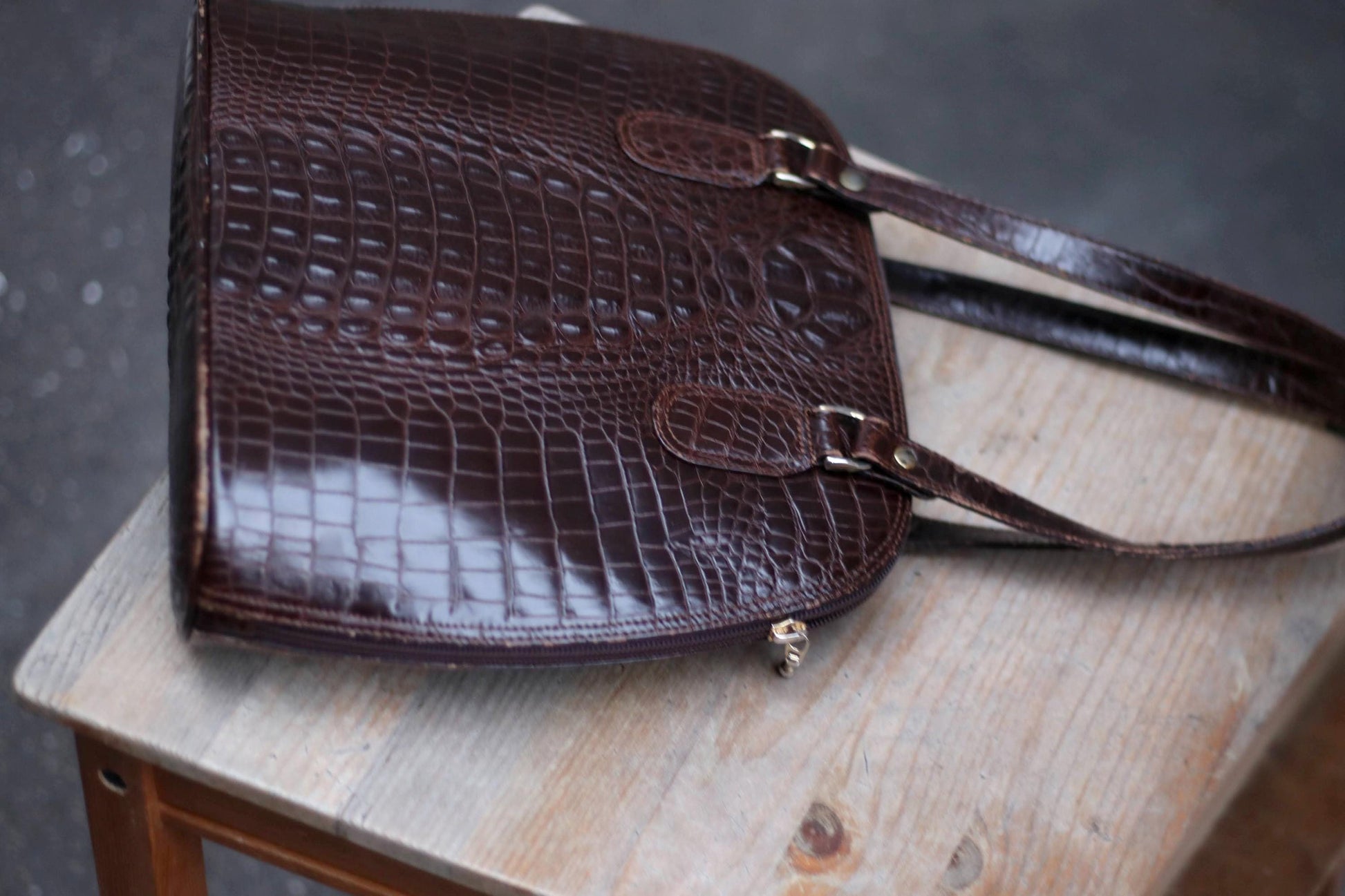 70s Vintage dark brown embossed leather shoulder bag on a wooden surface.