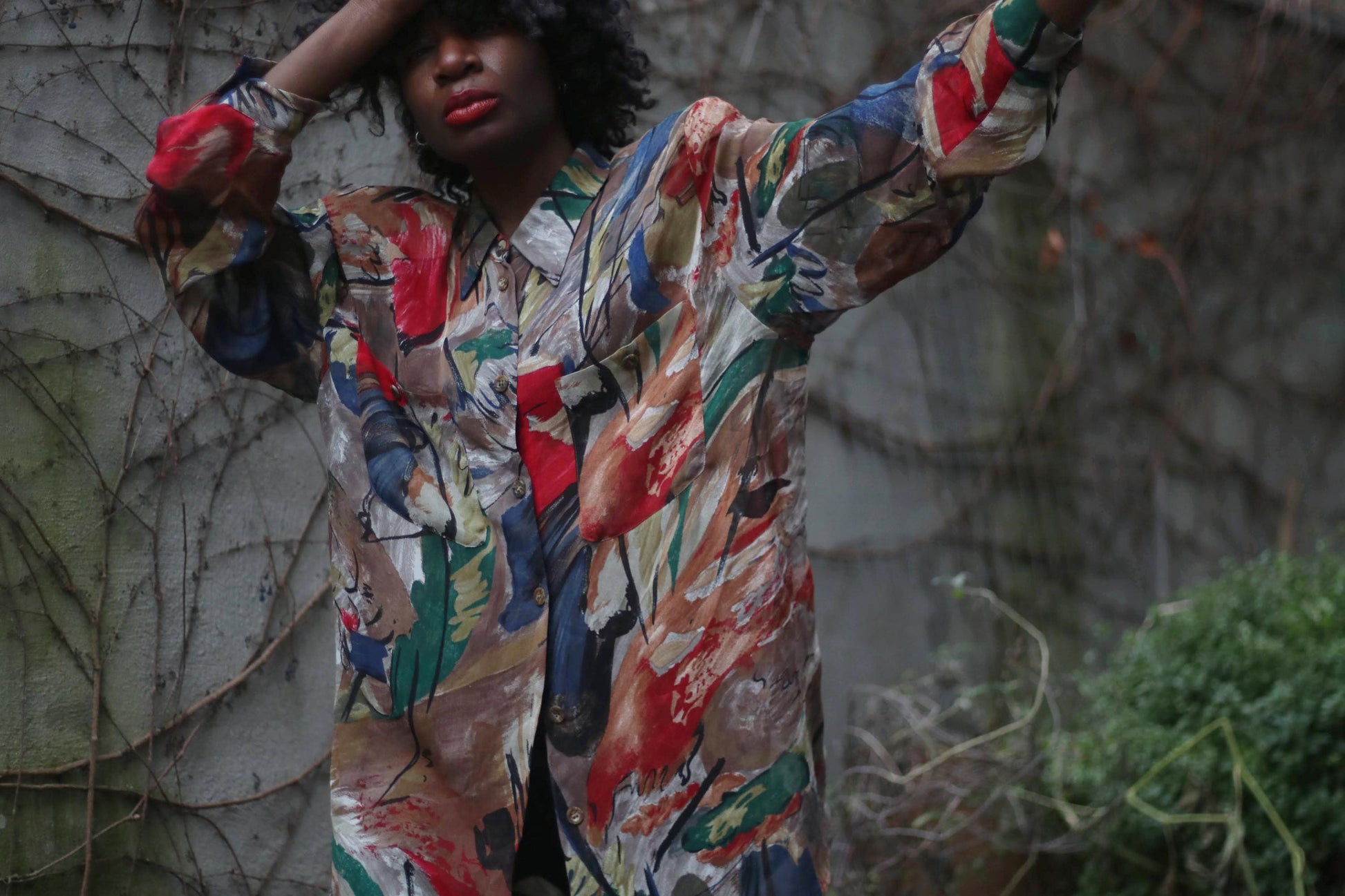 A fashion-forward person with voluminous curly hair and red lips showcases a vintage Gerry Weber abstract print blouse.