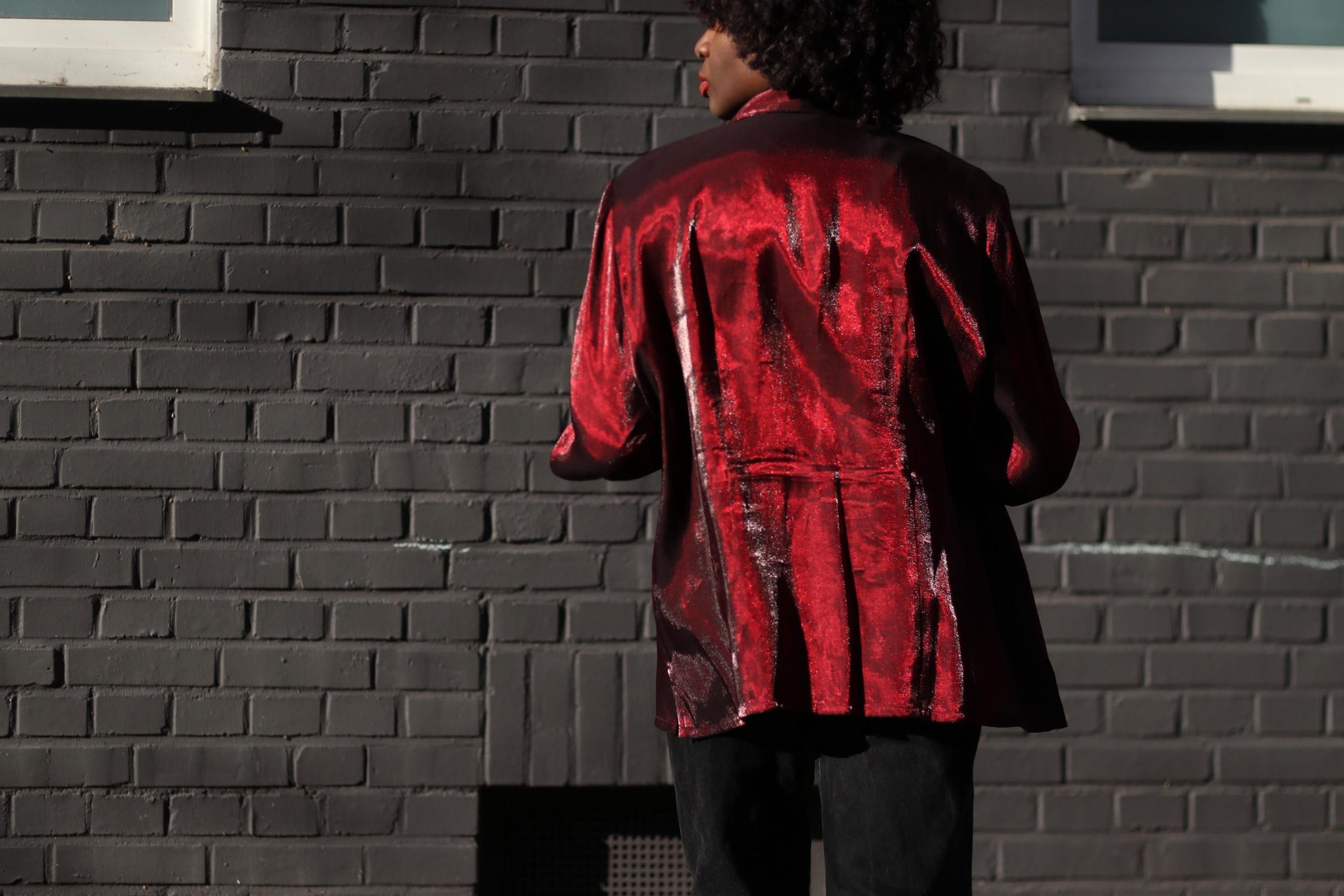 High-shine vintage blouse from the early 200s with structured shoulders and dramatic sheen styled on a female model with curly black hair. The image captures model from the back and showcases the button-up design as perfect for a statement outfit.