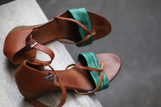 Vintage Italian leather sandals with green and brown straps, elegantly displayed on a rustic wooden table, exuding boho summer charm