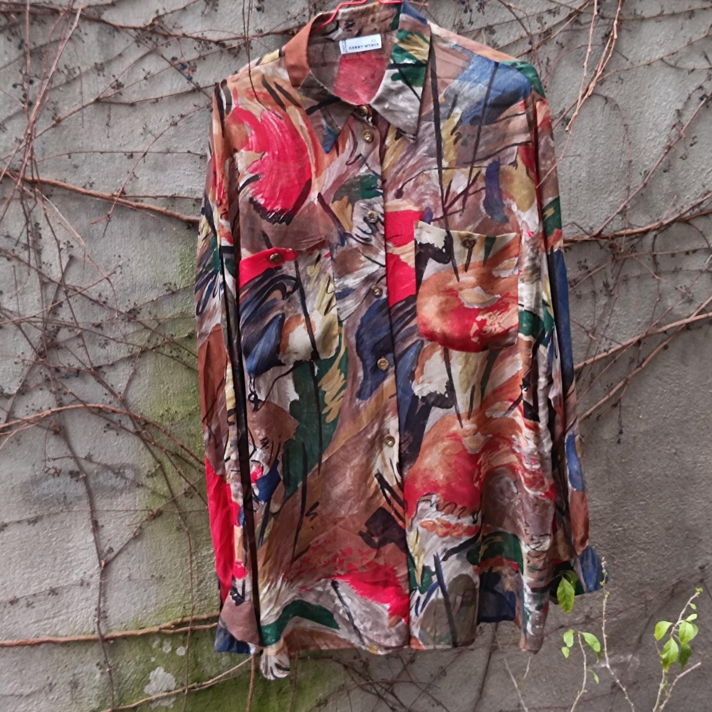 Close-up shot of an oversized vintage Gerry Weber blouse with an abstract painterly print. The 90s blouse features a vibrant mix of colors that contrasts beautifully with the natural outdoor setting.