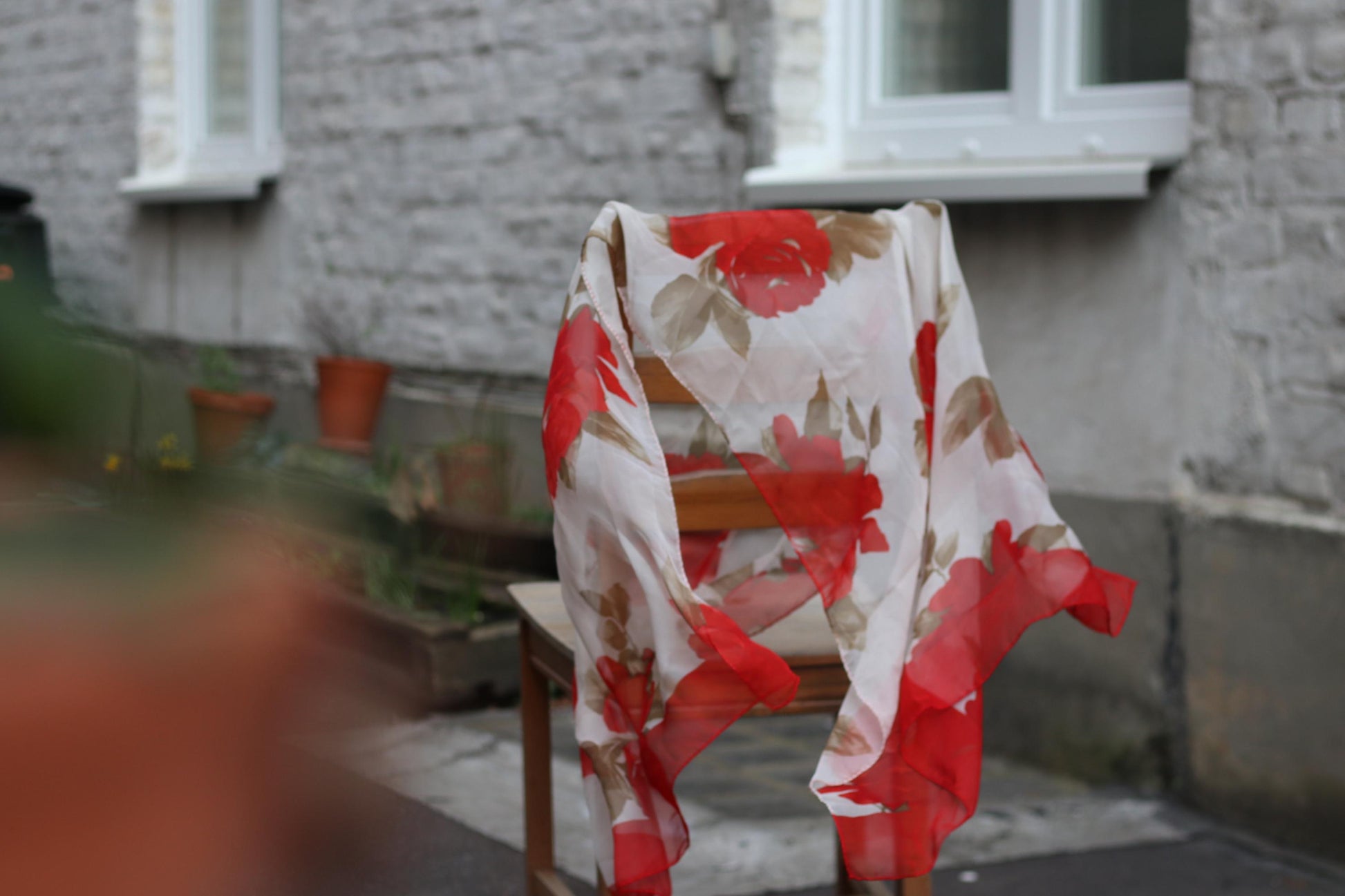 Vintage Escada silk scarf with red floral design, draped over a wooden chair in a minimalist outdoor setting.