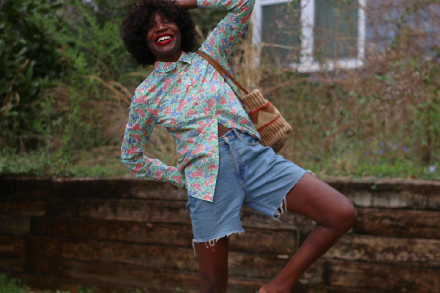 Capturing cottagecore charm, a woman showcases a vintage J.Crew floral print shirt. The cotton blouse features a button-up front and pointed collar, its soft pastel florals exuding a nostalgic, garden-inspired feel against a green background