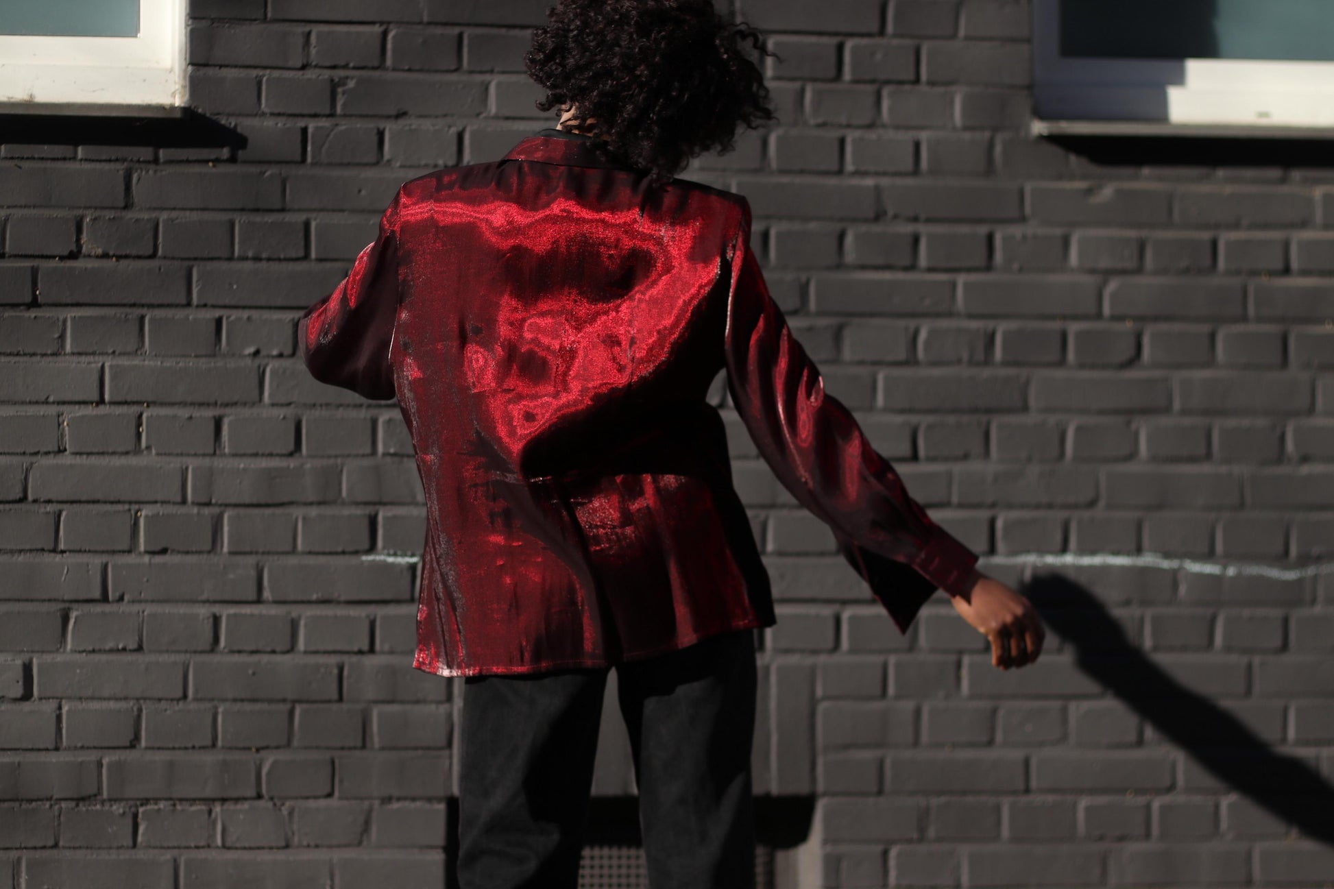Vintage 2000s metallic red blouse styled on a female model with black pants, giving edgy and futuristic vibes. The photo captures the model from the back