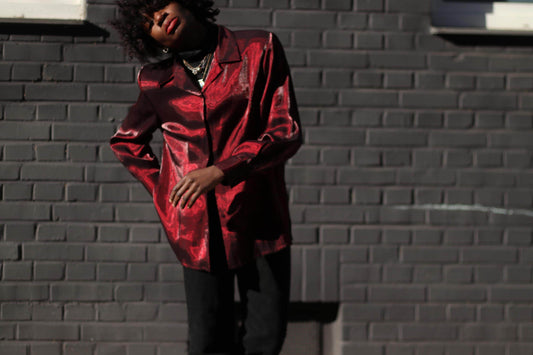 Female Model wearing a glossy red Y2K vintage blouse against a dark brick wall in direct sunlight.