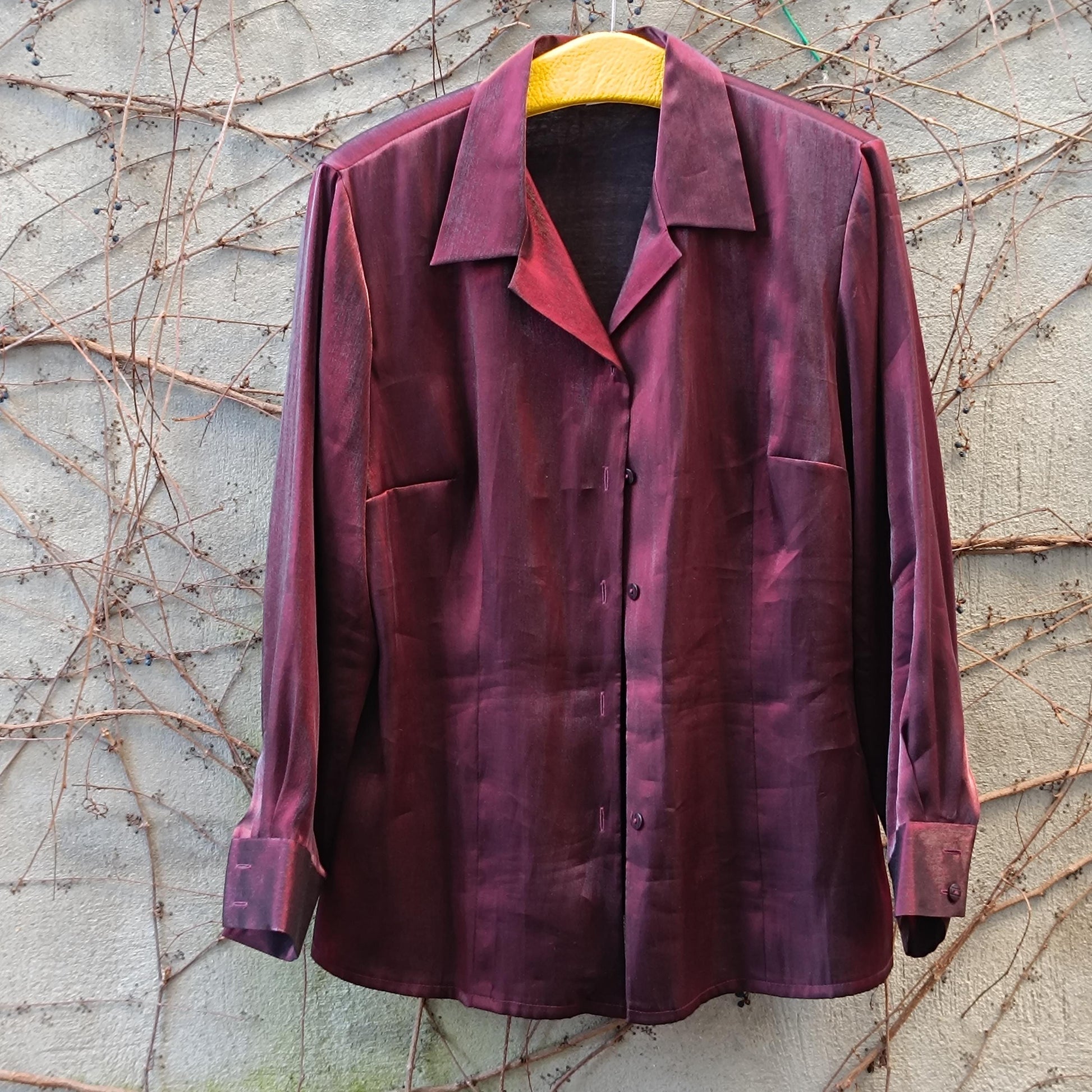 Vinesge glossy red Y2K blouse photographed hanging from a yellow hanger against a light brick wall covered in brown twines