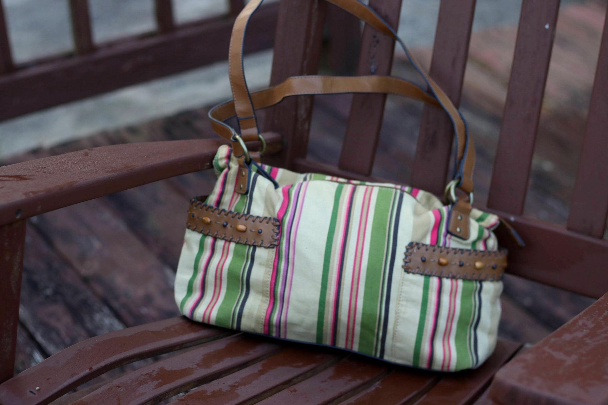 Vintage shoulder bag with striped pattern and leather strap, angled view on a rustic chair.