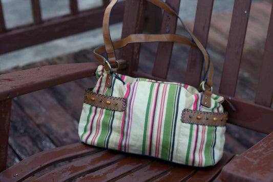 Vintage shoulder bag with striped pattern and leather strap, angled view on a rustic chair.