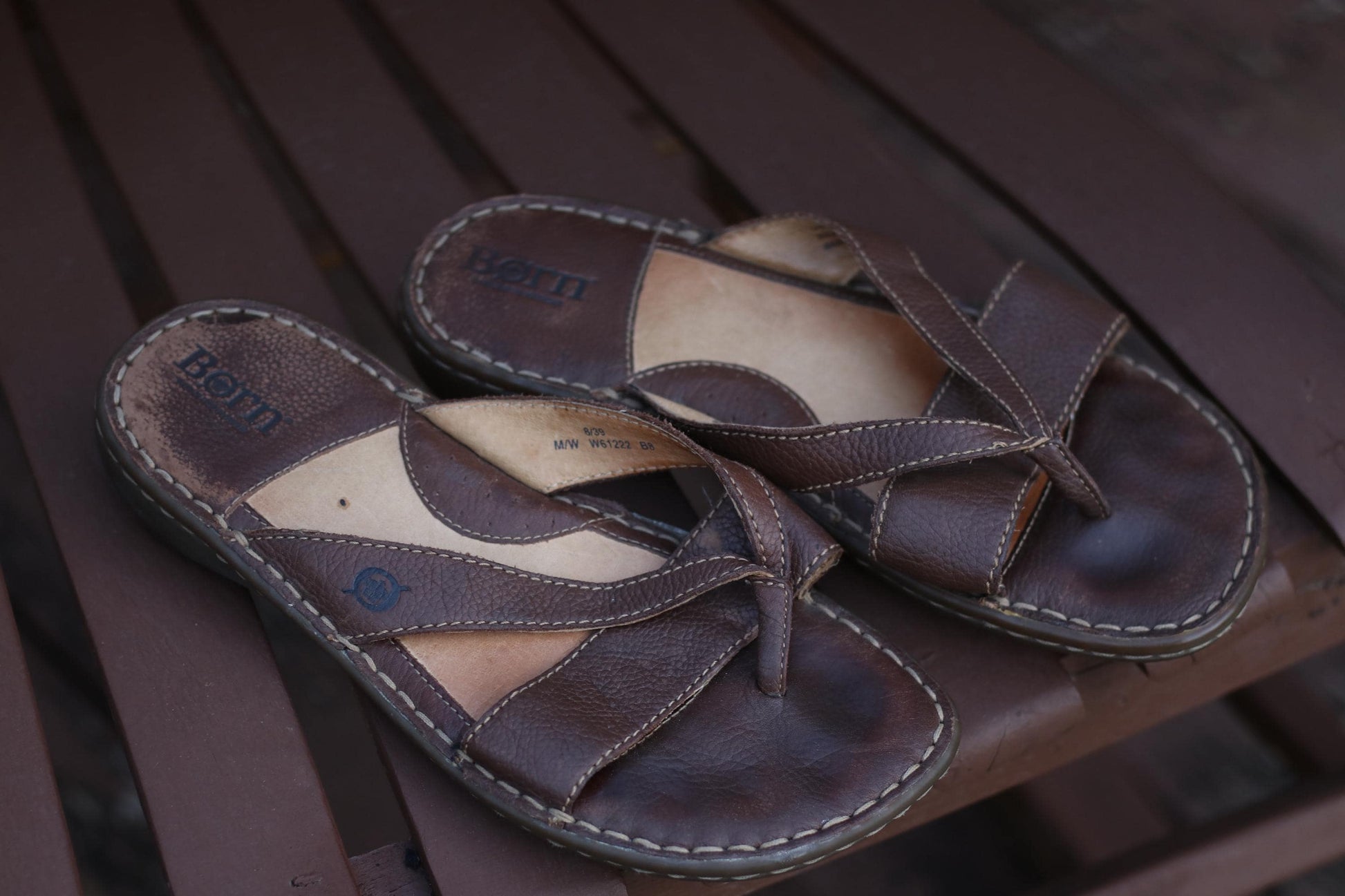 Vintage 90s Børn women&#39;s brown leather sandals with unique cross-foot straps photograhed outdoors on a brown wooden chair