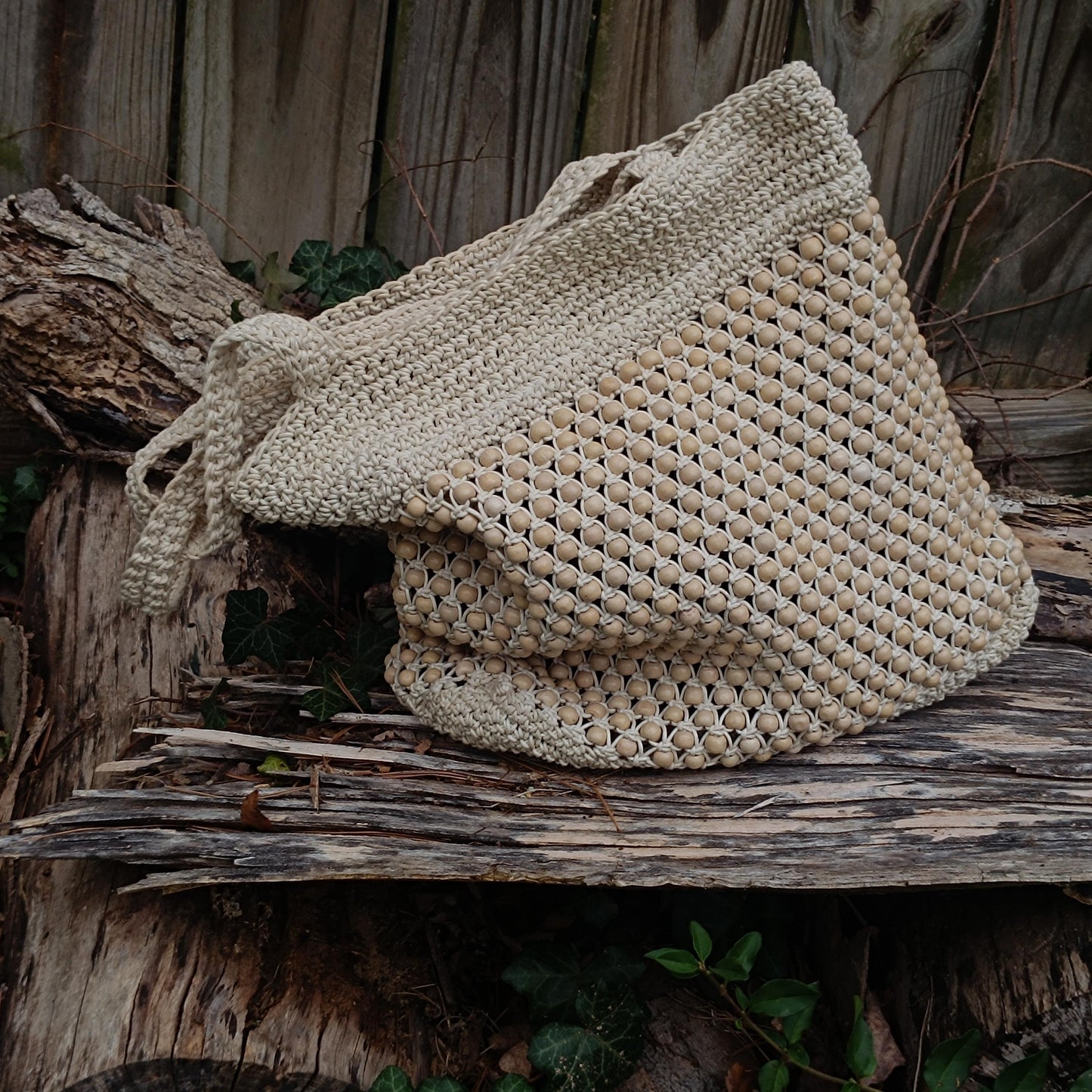A vintage 90s Madewell tote bag featuring woven raffia with intricate wooden bead detailing, resting on a rustic log with green ivy in the background.