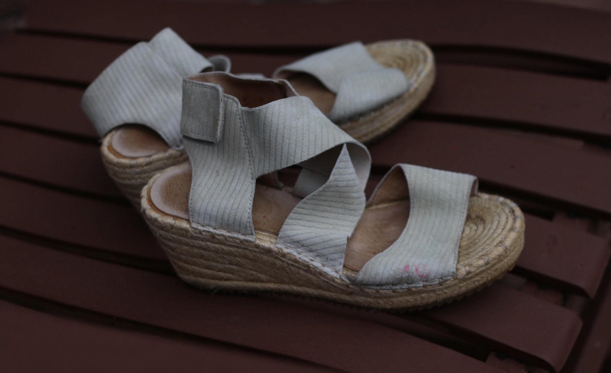 Vintage 90s Eileen Fisher  espadrille wedges in soft grey, featuring crisscrossing straps, an adjustable Velcro ankle strap, and a natural jute platform wedge heel, resting on a brown wooden surface.