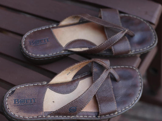 Comfortable handcrafted 90s Børn designer sandals with a relaxed, broken-in aesthetic. The vintage flip flops are photographed on a wooden brown chair outdoors.