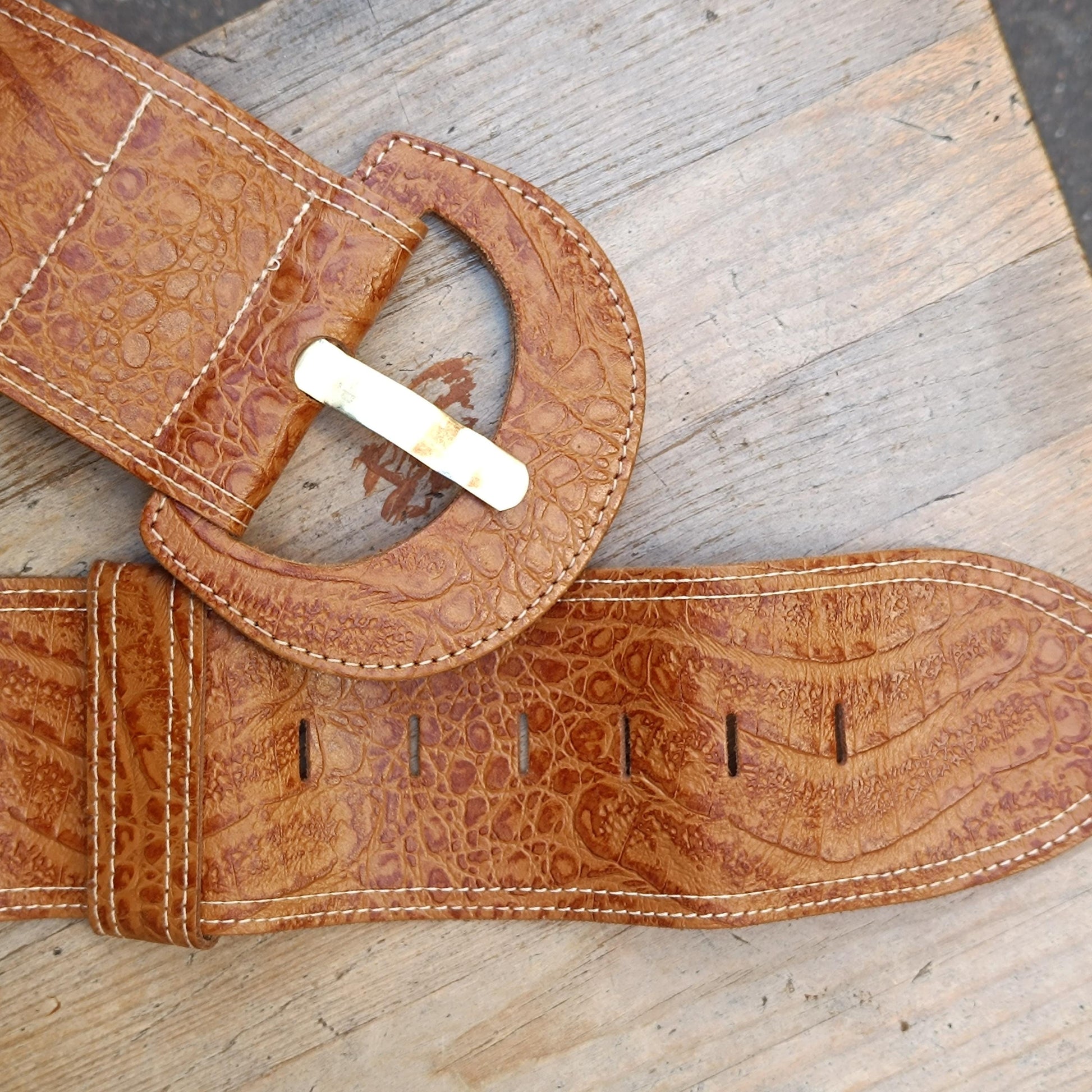 Vintage Brown Handmade Leather belt with an oversized silhouette and statement brass buckle is photographed on a rustic wooden background. Focus is on the big buckle and the faux exotic finish of the belt