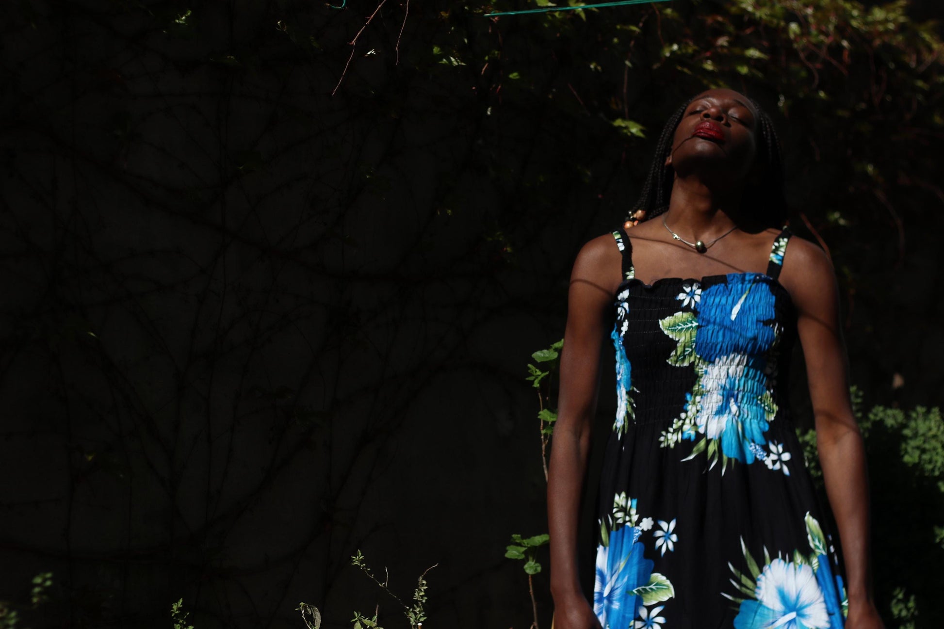 Outdoor fashion shot of a female model  wearing a vintage 90s  lightweight rayon sundress with a bold black background adorned with oversized blue and white flower patterns. The dress has thin straps and a relaxed, flowing silhouette, giving off an Hawaiian summer vibe.
