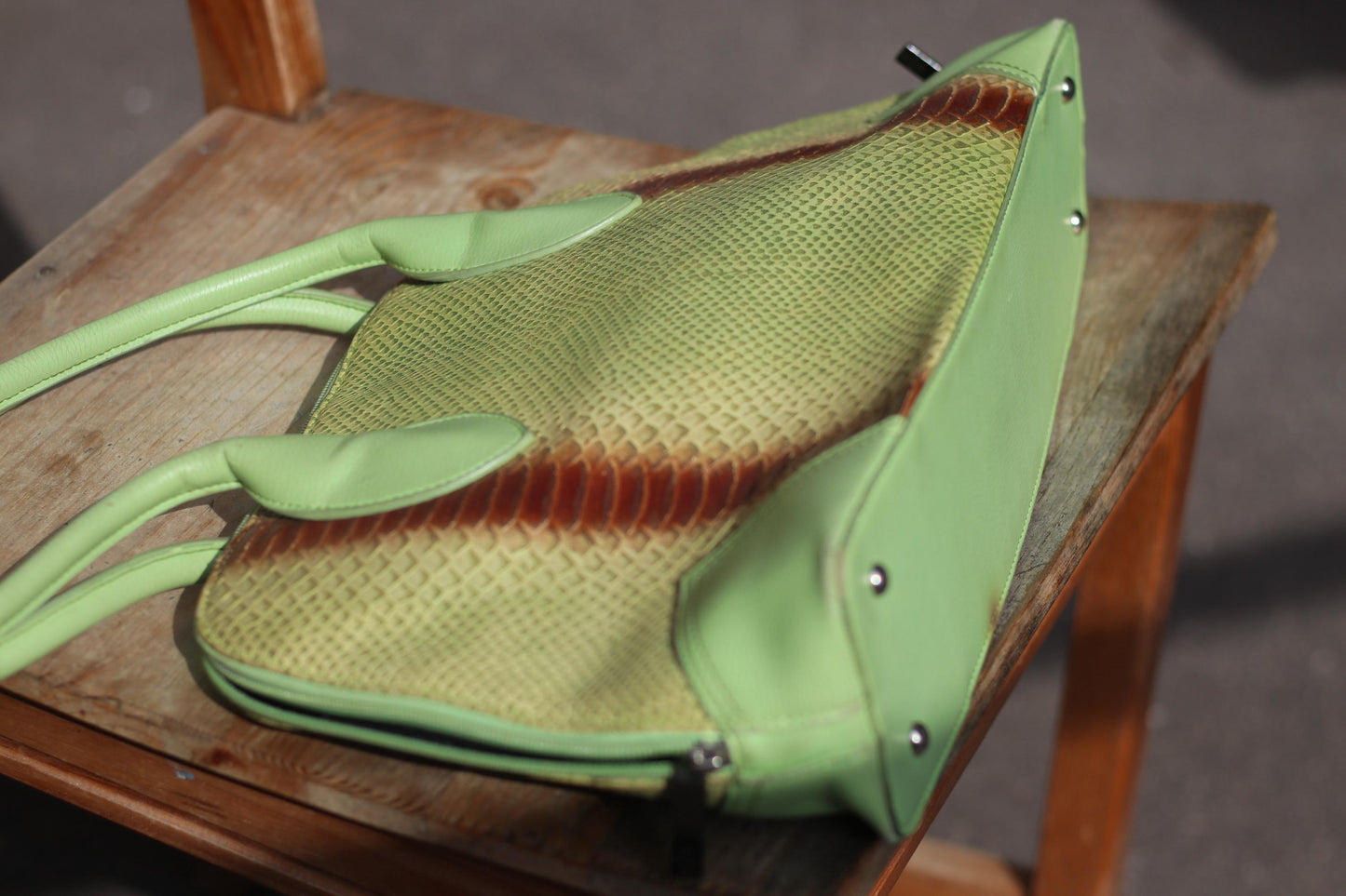 A tilted angle shot of an 80s vintage, light green faux leather handbag featuring an animal print stripe in brown and reddish tones, highlighting its shape, rounded handles, and metallic stud details on the side.