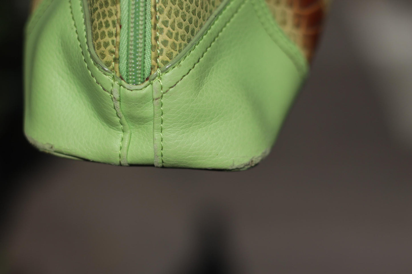 A detailed close-up of an 80s vintage, light green faux leather handbag featuring an animal print stripe in brown and reddish tones, The image focuses on the wear at the bottom, showcasing it&#39;s vintage charm for the modern woman
