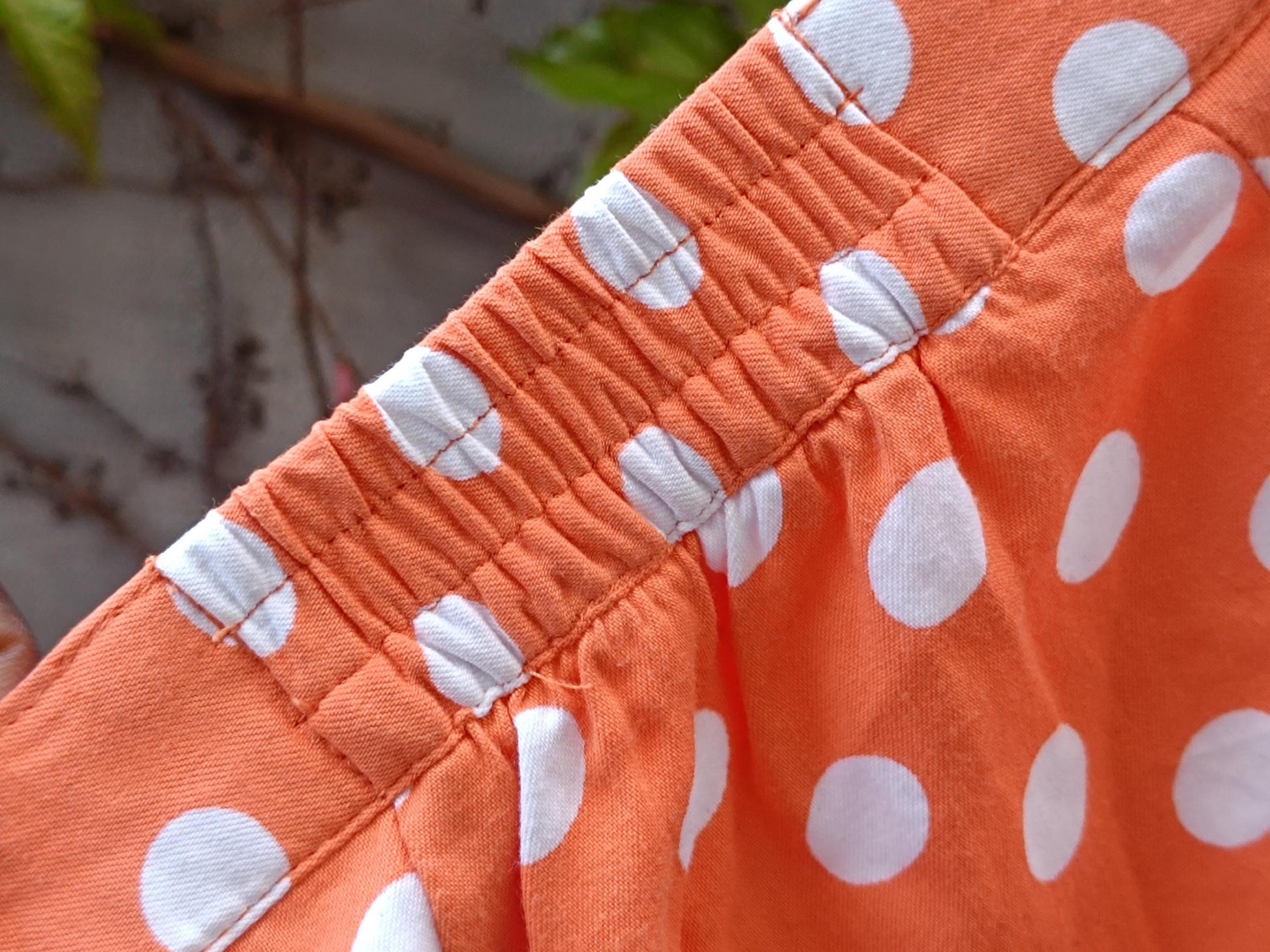 A close-up image of a chic French Flair 90s Polka Dotted Skirt in Orange. The photo highlights the colour, and half elasticated waist of the whimsical mini summer skirt