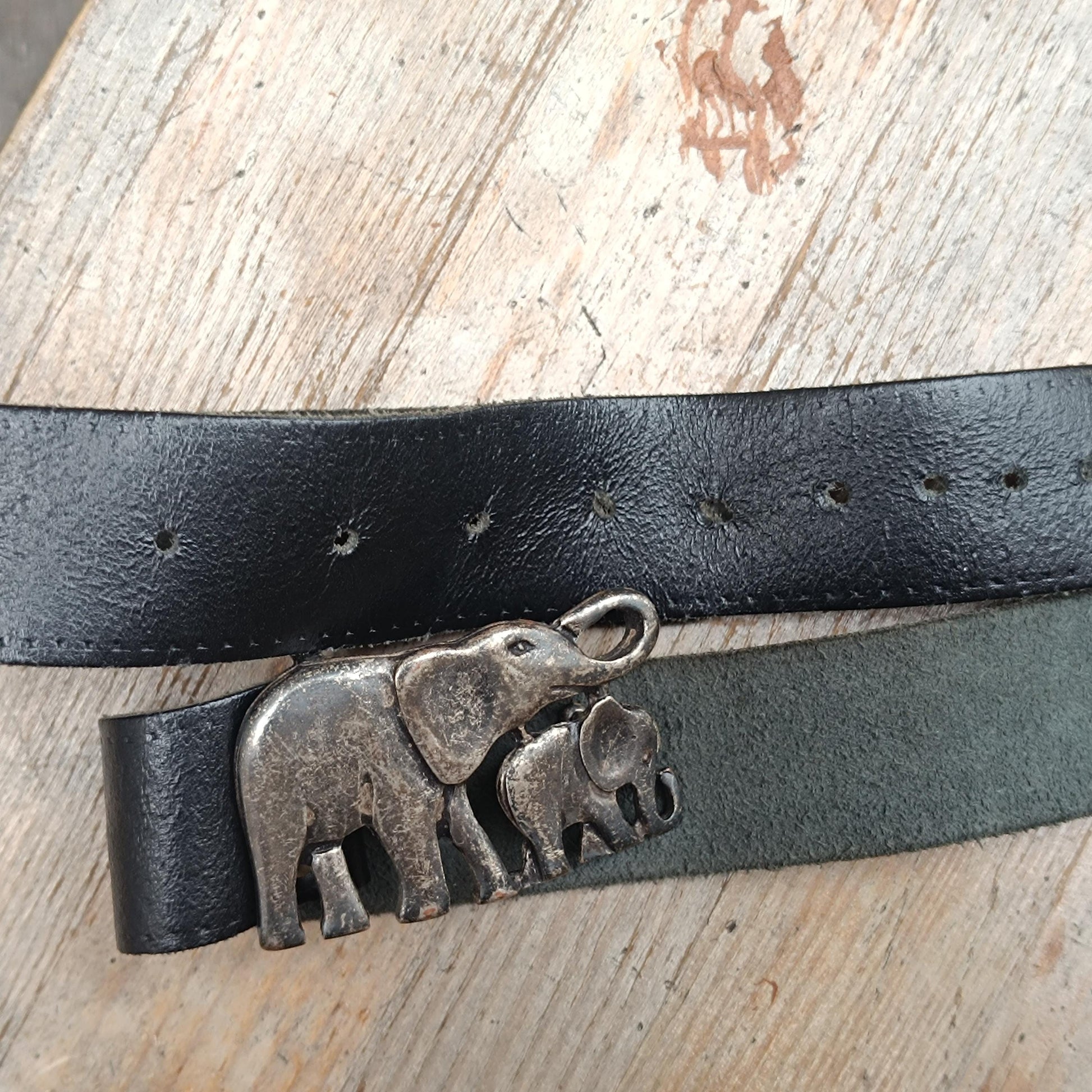 Artistic flat lay image of a vintage black leather with a silver-toned elephant buckle belt captured on a wooden surface,