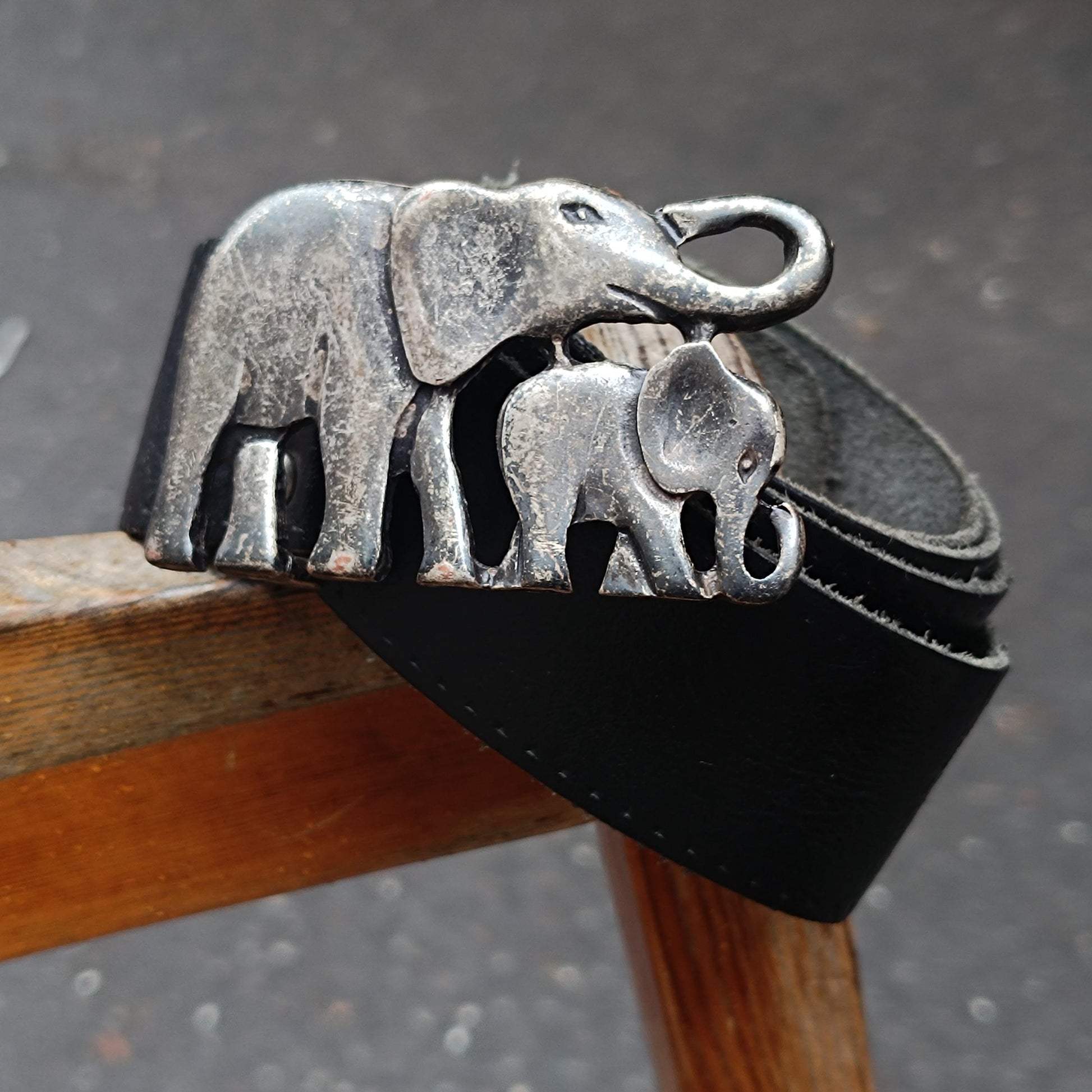 Detailed image of a vintage handmade leather belt with a  mystical elephant buckle photographed on the arm of a wooden rustic chair