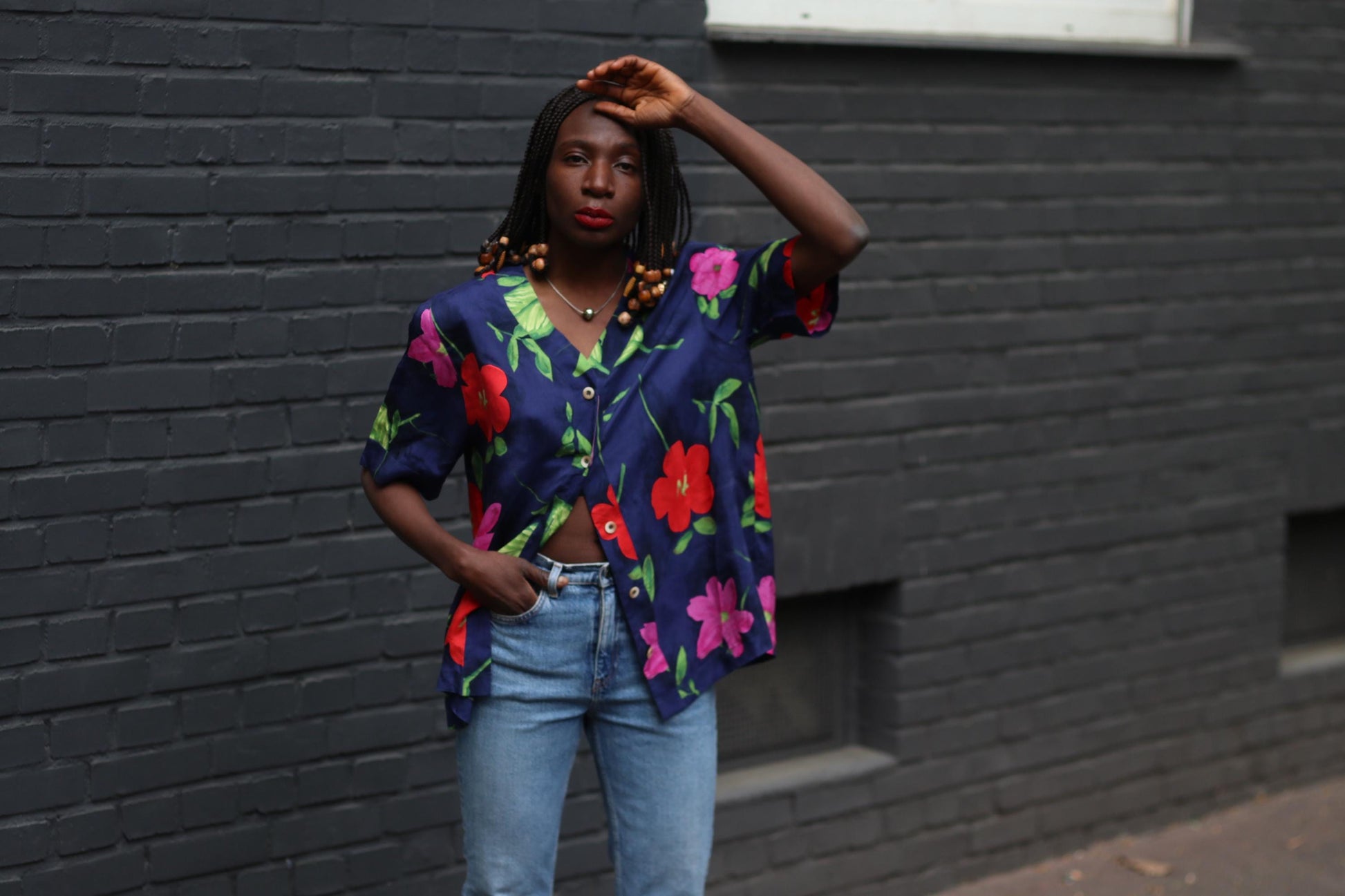 Front view of vintage navy floral blouse with bold hibiscus print on a model styled with blue jeans. The model has one hand in her pocket and the other up, as if ready to wave.