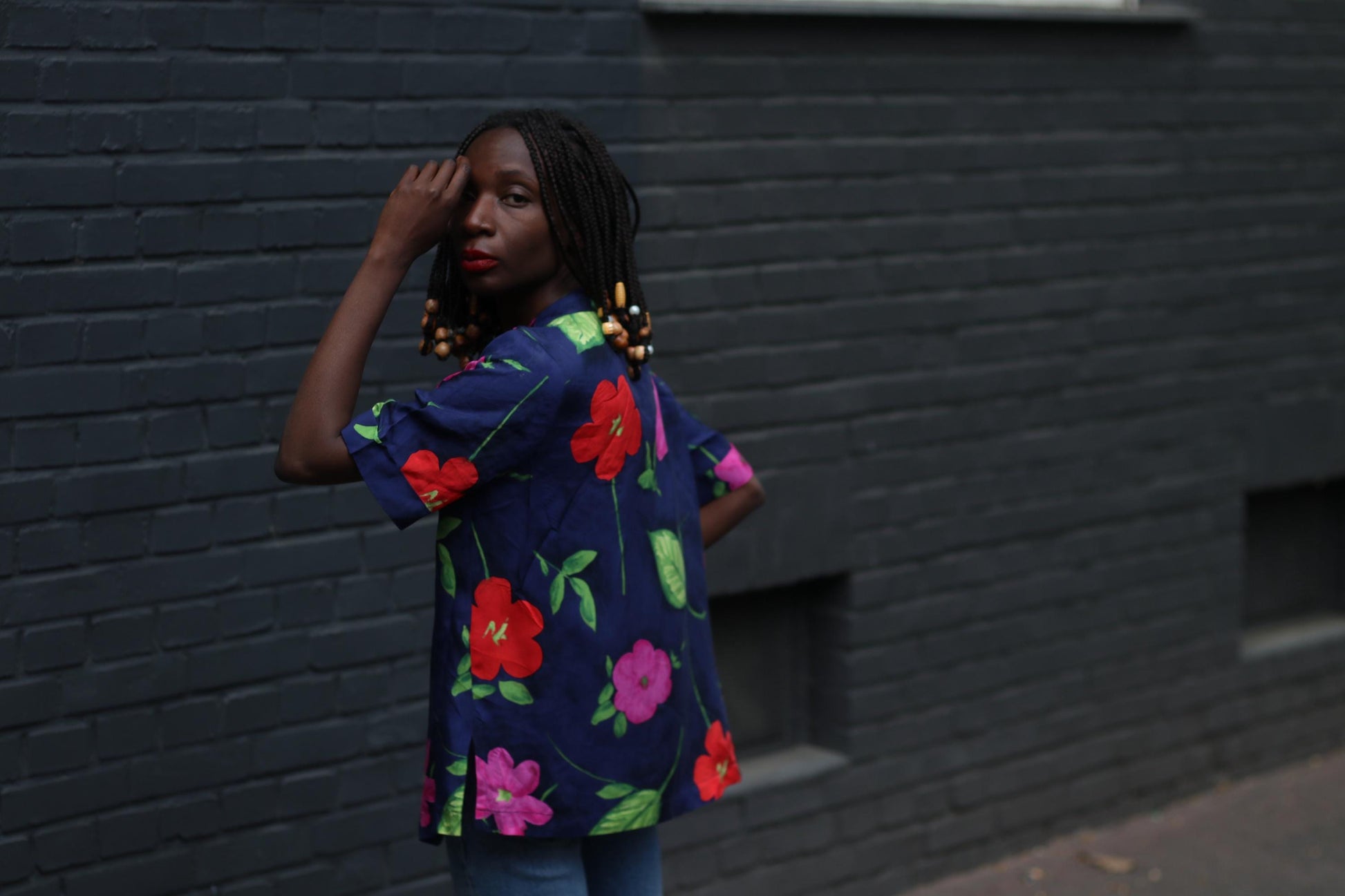 Side view of model in a vintage navy floral blouse with bold hibiscus print photographed infront of grey wall which highlights the bold  Hawaiian-like Print of the  Button-Down Shirt