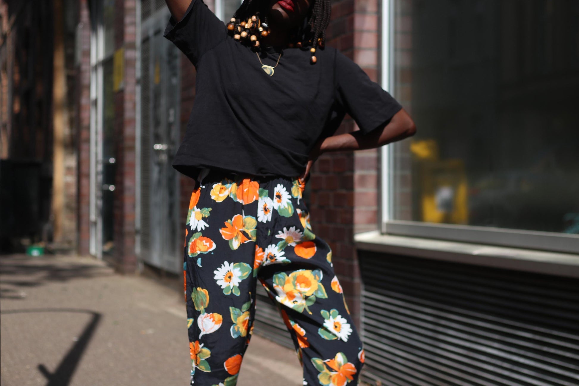 Detailed view of a vintage black capris from the 90s with bold orange and white floral prints, paired with a simple black t-shirt shot on a model face cropped out and one hand on hip.