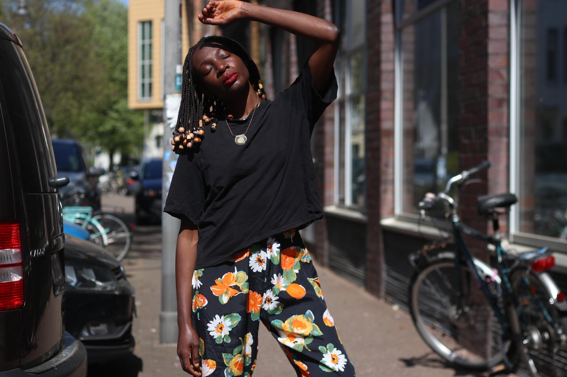 An artistic portrait of a model with beaded braides, wearing a pair of vintage boho floral capris with black t-shirt,  with her eyes closed, hands raised to the sun she exudes a carefree spirit perfect for summer festivals