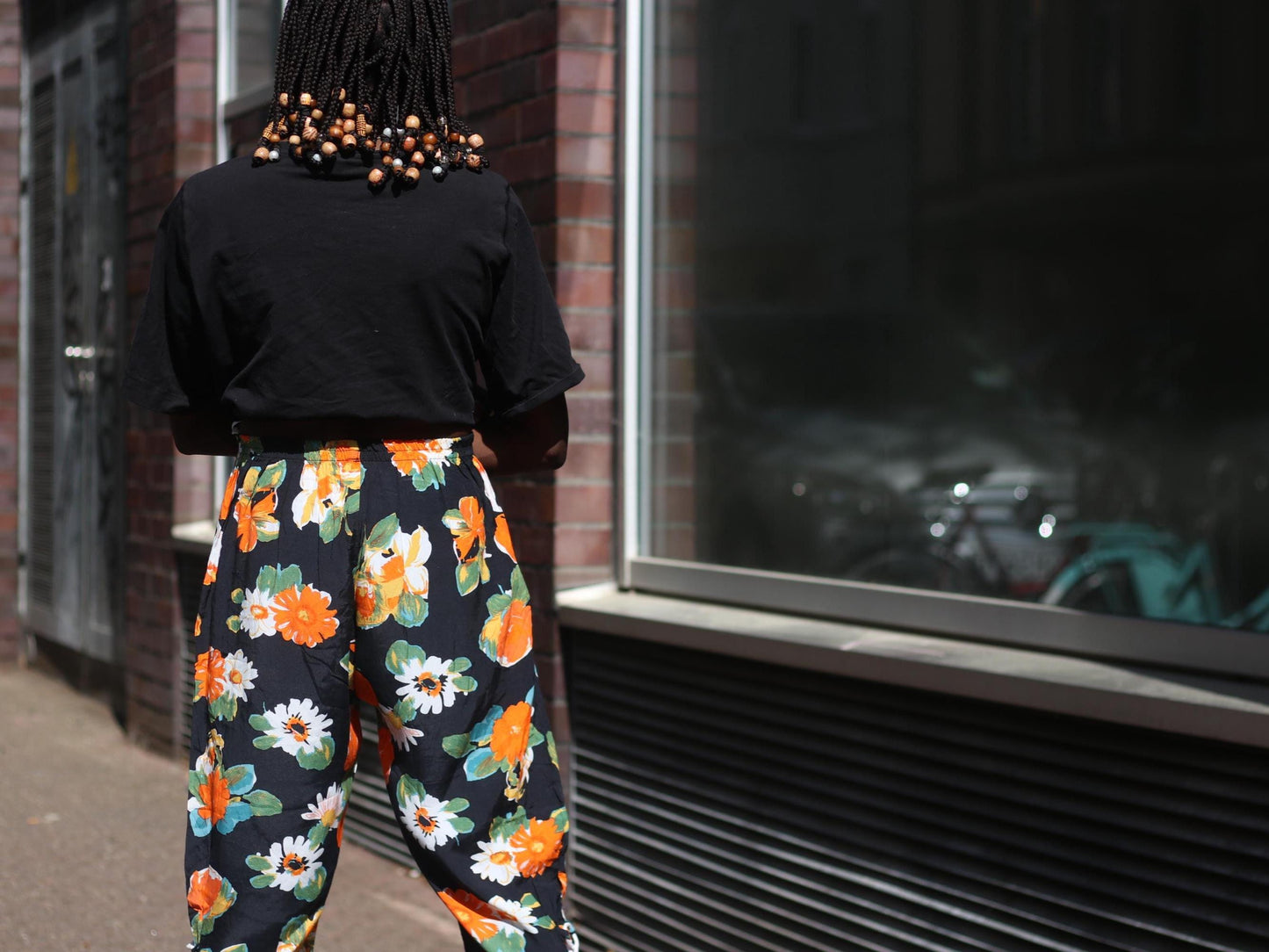 Back view of vintage daisy print capri pants with high-waist elastic, styled casually with a black tee on a female model on a sunny urban sidewalk.