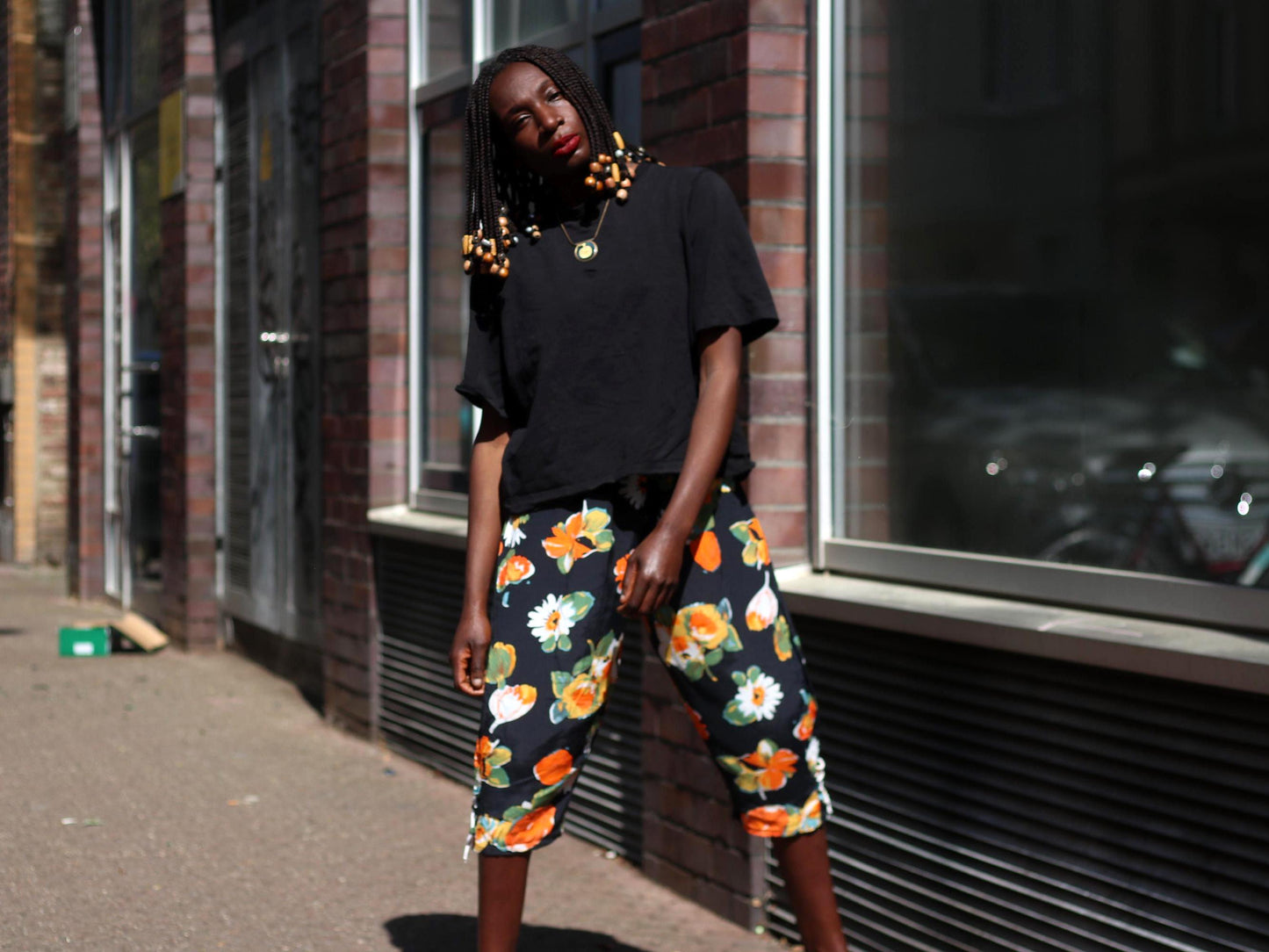 Bold floral vintage capri pants worn casually with a loose black tee on a female model with beaded braided hair , styled for warm weather with a mix of cottagecore and 90s fashion vibes.