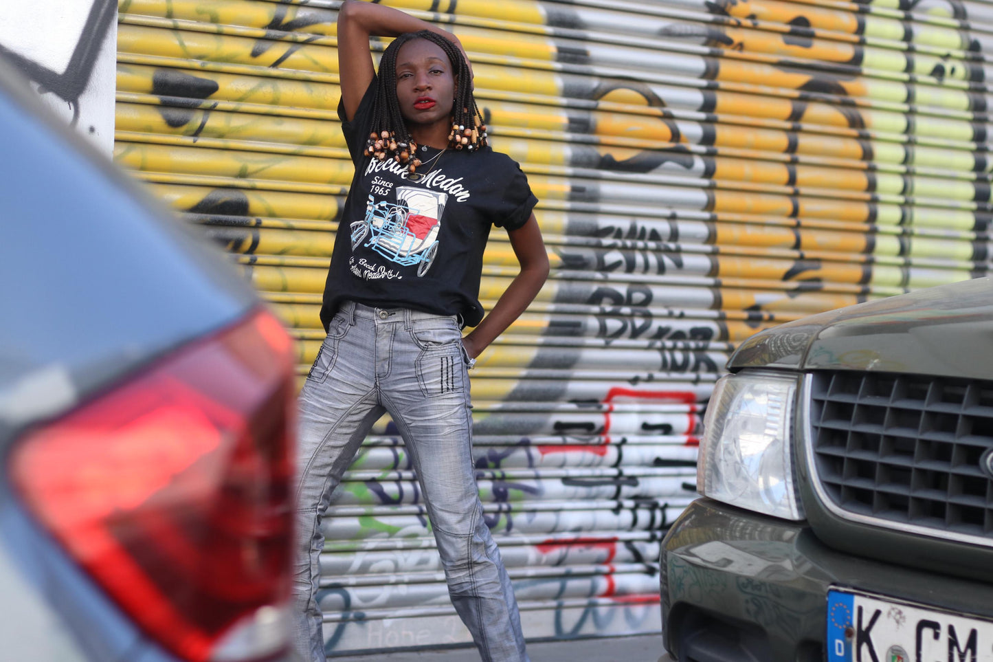 Female model wearing a vintage Y2K silver moto jeans with metallic sheen, straight-leg cut, and detailed paneled construction with a graphic T-shirt photographed in front of a graffiti covered wall