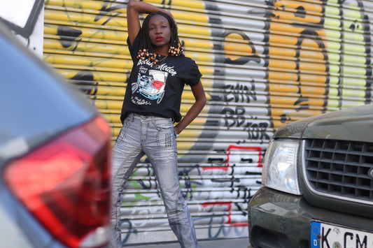 Female model wearing a vintage Y2K silver moto jeans with metallic sheen, straight-leg cut, and detailed paneled construction with a graphic T-shirt photographed in front of a graffiti covered wall