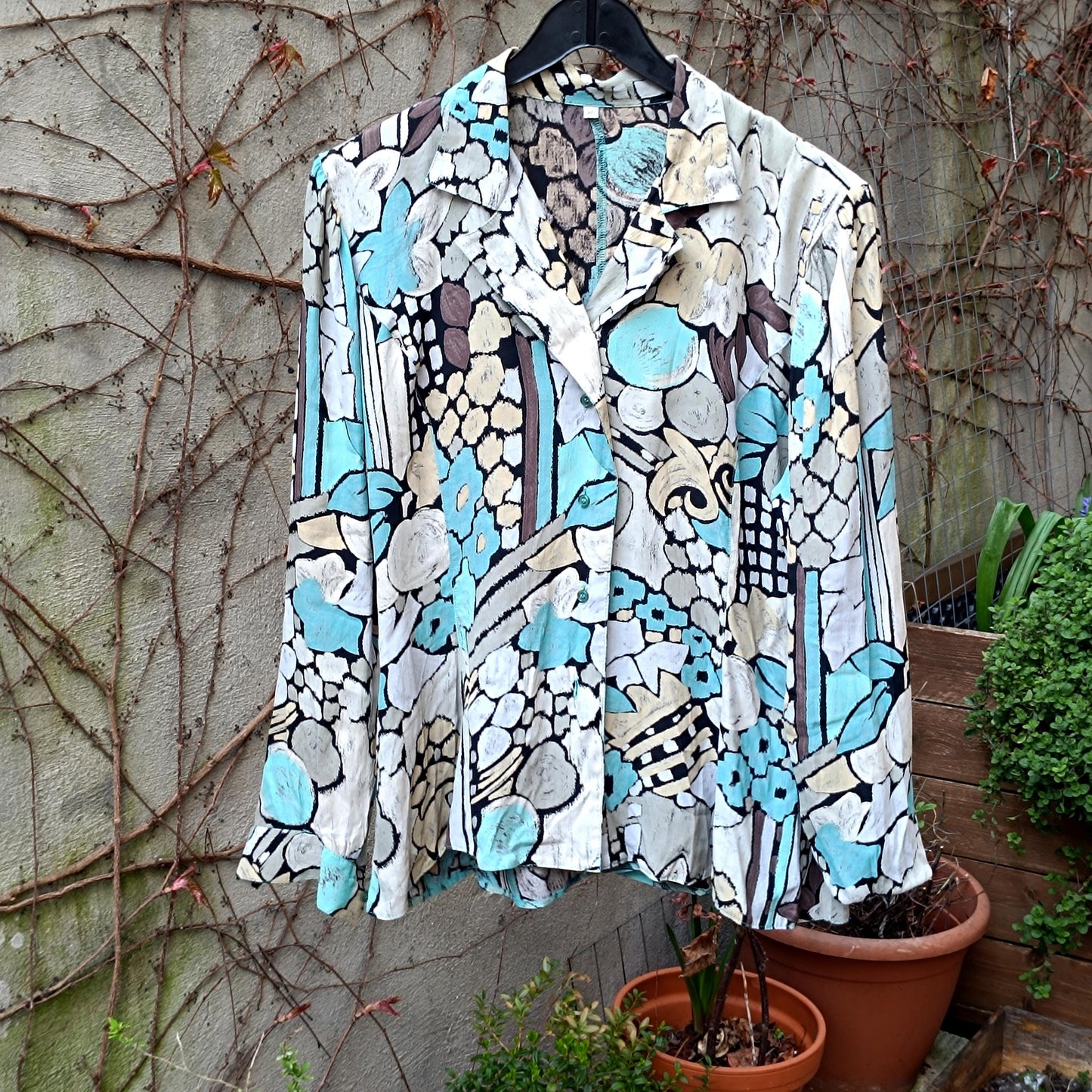 Vintage 90s Viscose blouse with abstract blue and neutral print, displayed on a hanger outdoors.