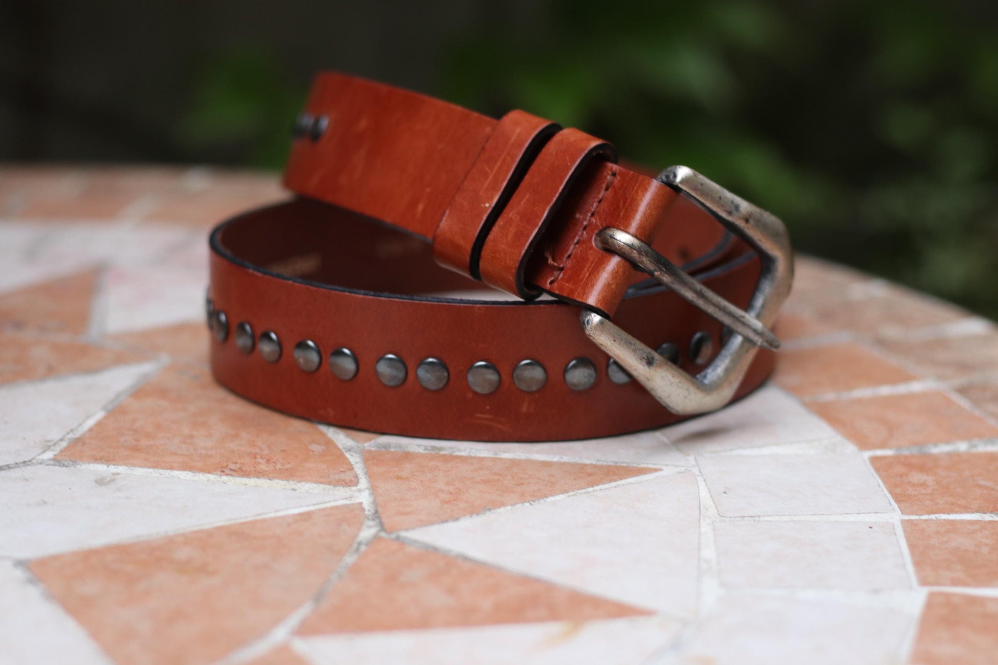 A brown vintage belt with a silver buckle and decorative studded details presented on a textured surface.
