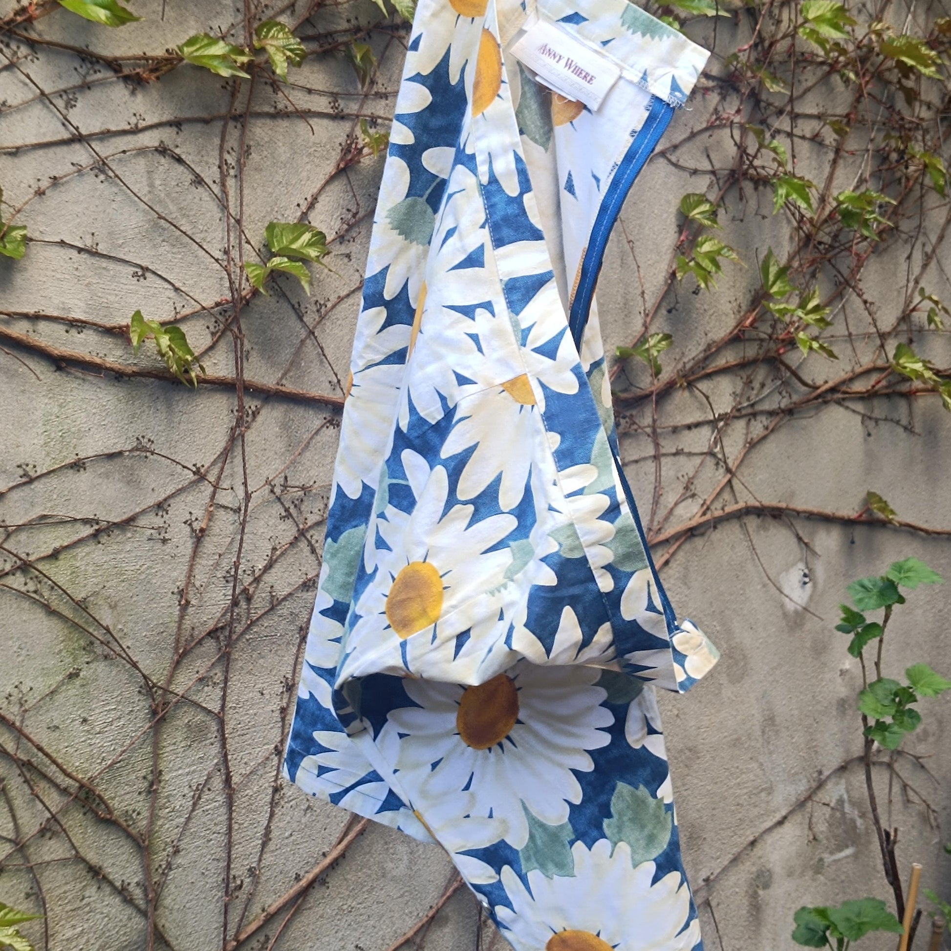 90s vintage blue and White Floral Print Skirt with a bold daisy print hanging on a clothing line in the garden against a walled background with browning ivy and twines