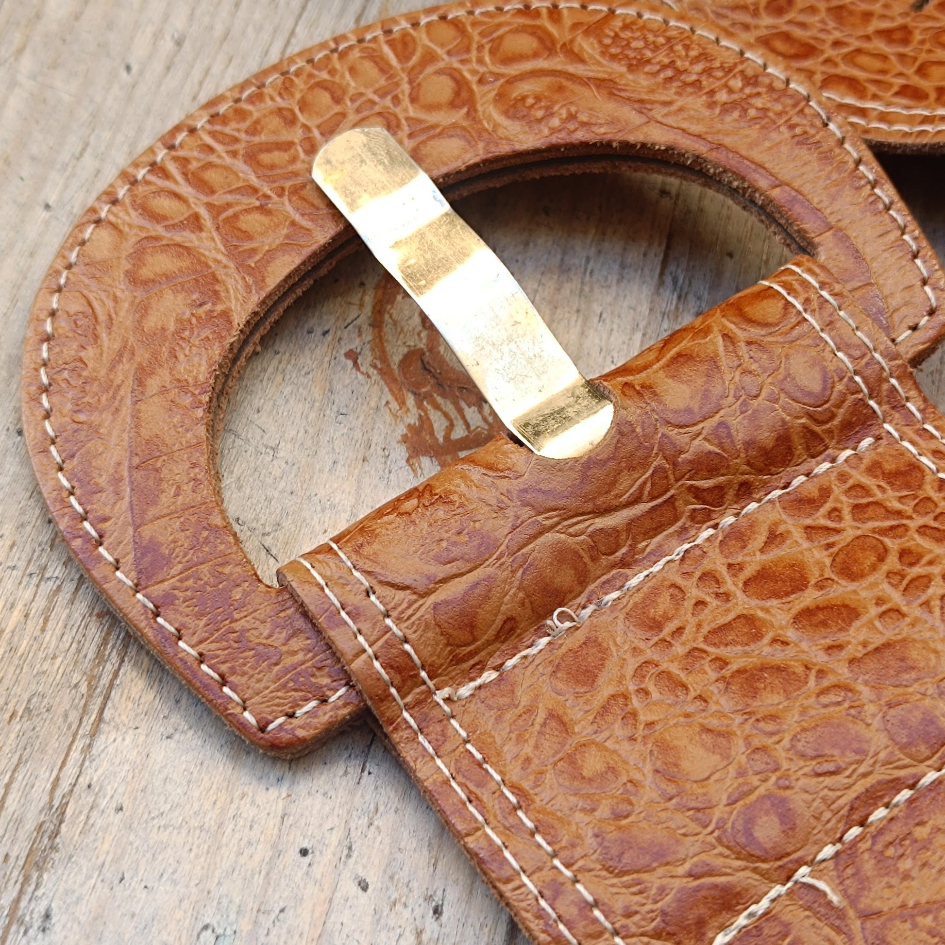 Close-up of the  brass buckle of a Boho- vintage adjustable belt made in the 70s from leather featuring antique brass hardware and stitched edges