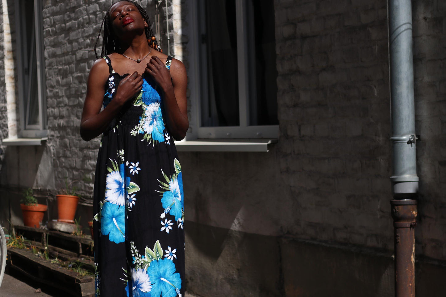 A Black individual models a sleeveless, ankle-length vintage rayon dress ideal for warm weather. The dress has a black base color with prominent, abstract-style blue and white floral patterns