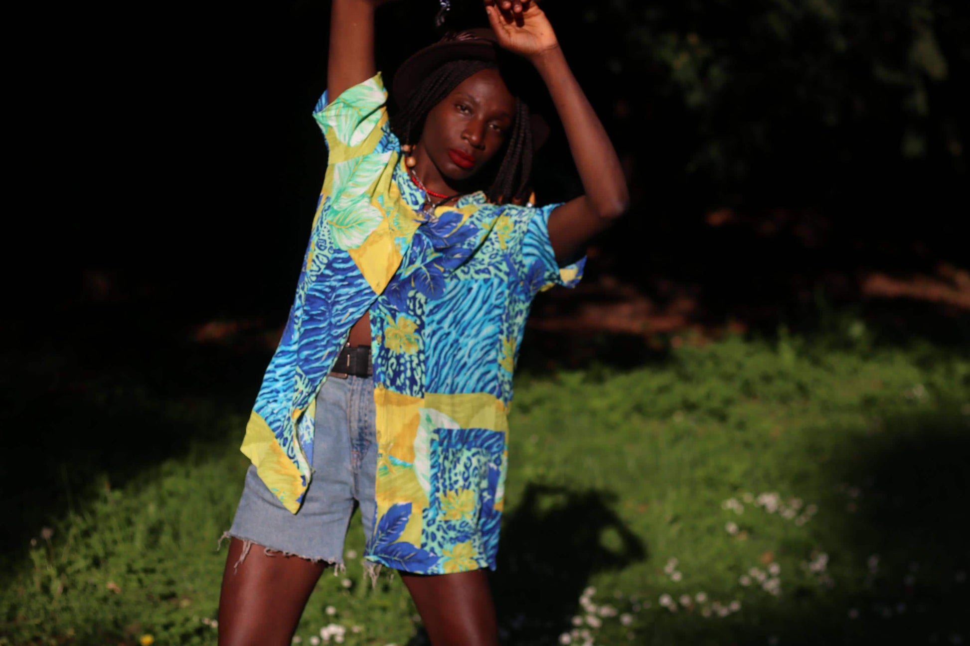 Vintage French tropical shirt with vivid blue, green, and yellow prints, styled casually on a model with beaded brown hair and denim shorts.