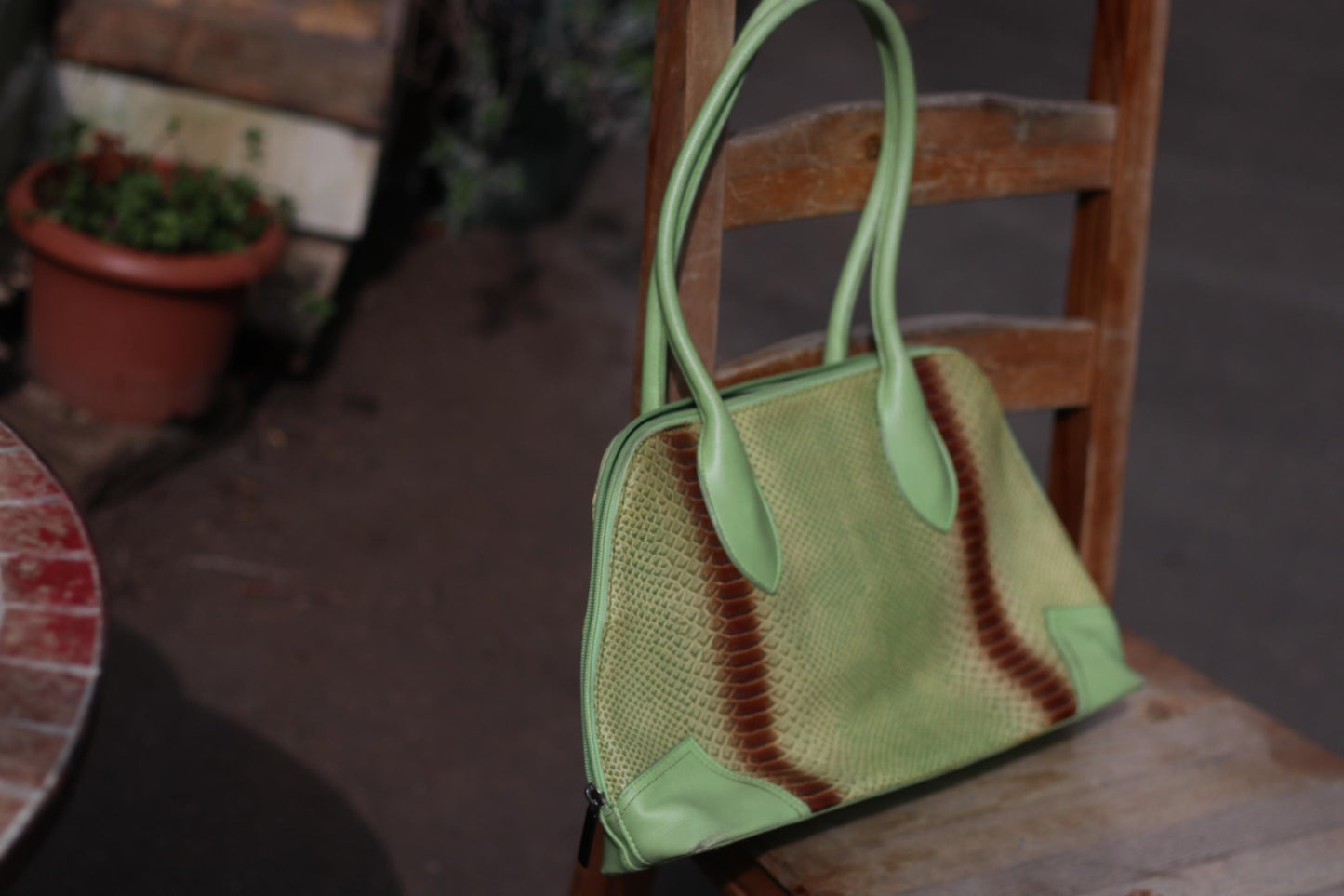 An 80s vintage, light green faux leather handbag with a striking animal print stripe, displayed on its side on a wooden chair, highlighting its metallic feet and retro design. The everyday design is very boho and retro chic, made for the fashion-forward woman