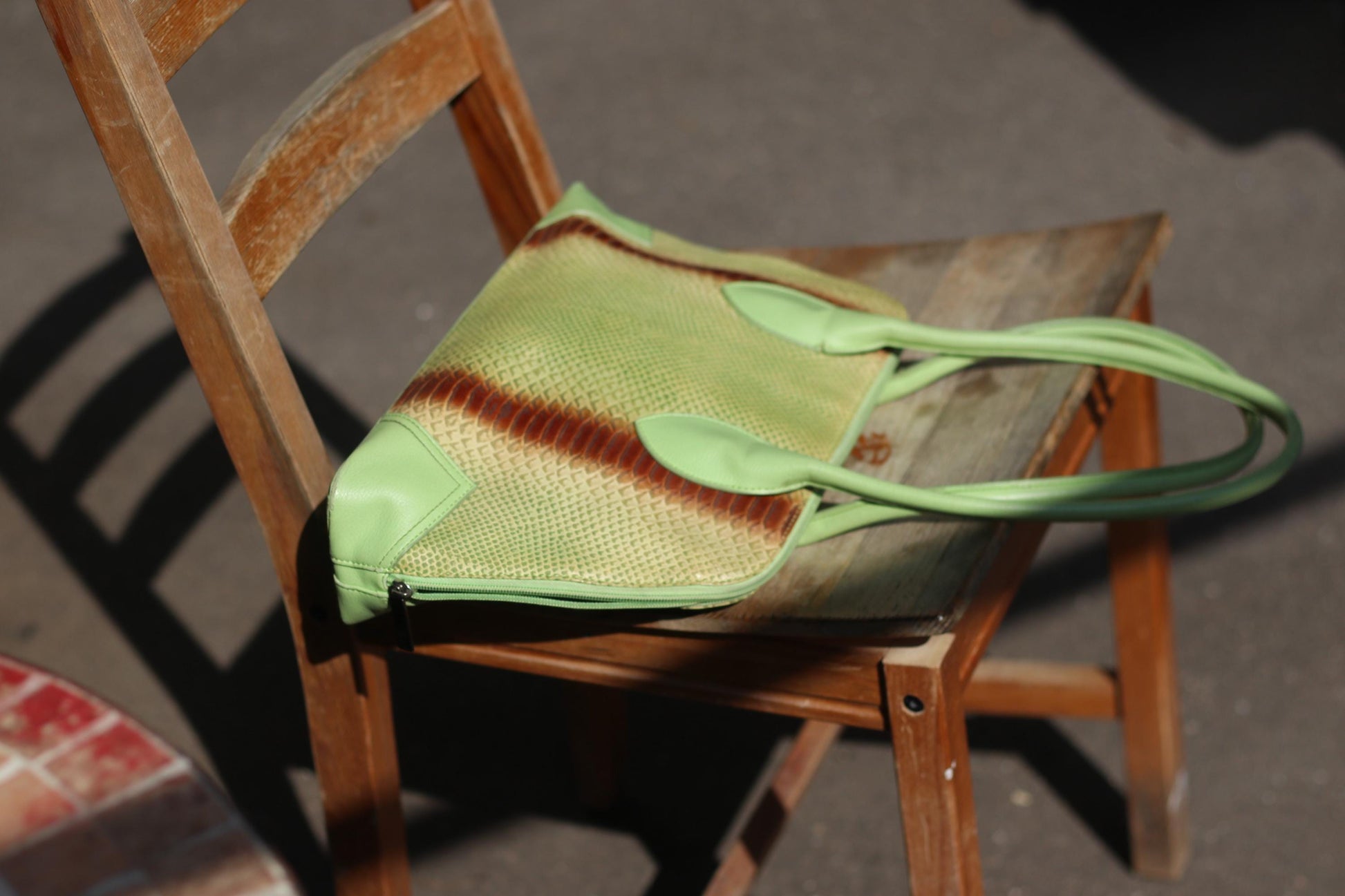 A fashion image of a vintage 80s green and  tote. The faux leather shoulder bag is light green with a statement  animal print stripe in browm. it is generous in size and can be carried on the shoulder bag. The bag is photographed on a wooden chair .