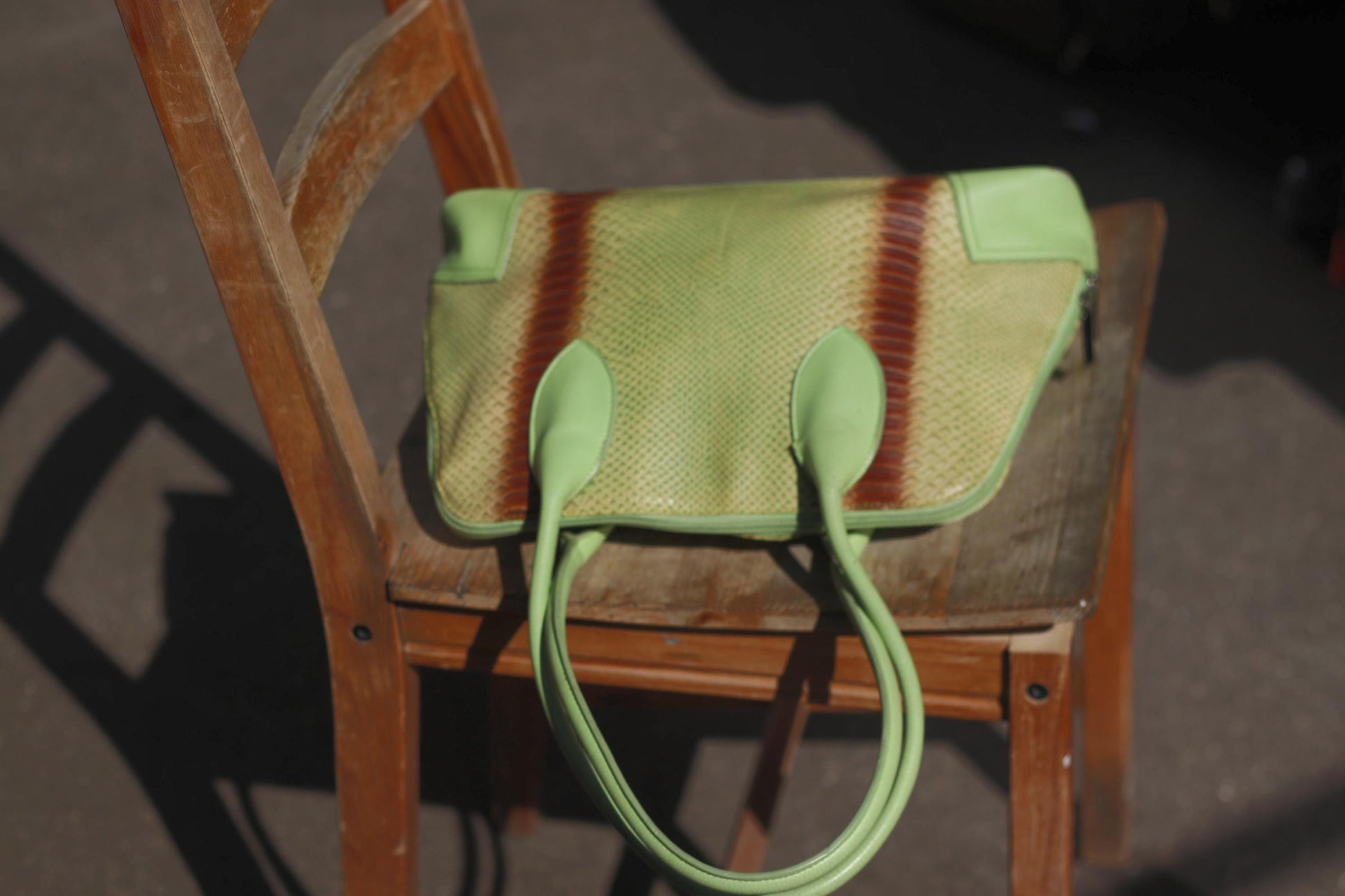 A vintage 80s, light green faux leather handbag with darker stripes, reminiscing of animal print resting on a wooden chair with a slatted back.