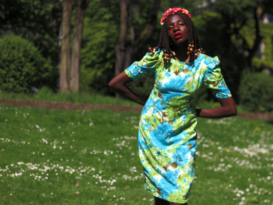 Handmade 1970s floral dress with puff sleeves and vibrant green and blue flower print, modeled  on a female with beaded braided hair and a floral crown photographed outdoors in natural light