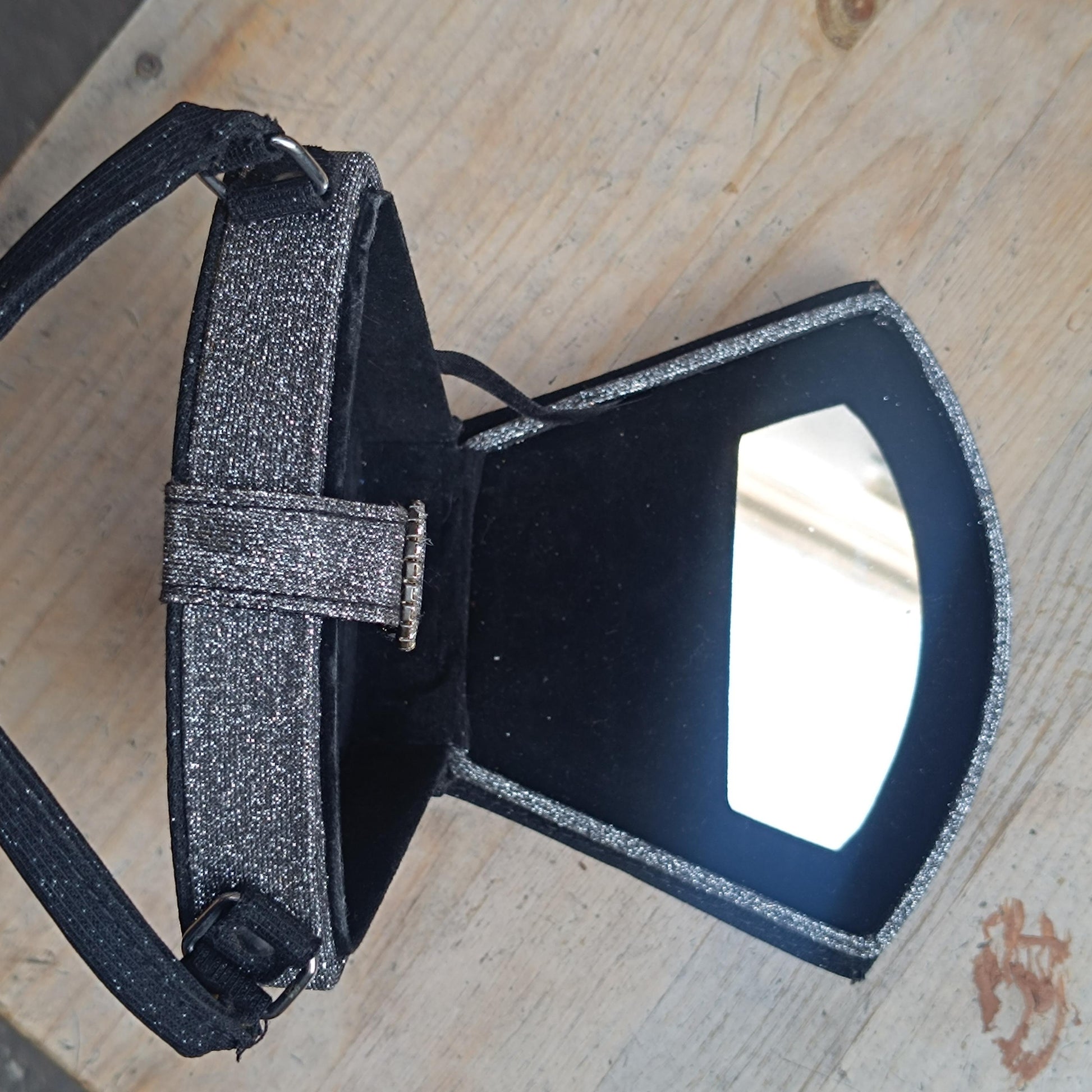 Vintage black glitter mini bag with top handle and faux-bling detail, laid flat  and open on a wooden surface .The small mirror inside the y2k bag is visible
