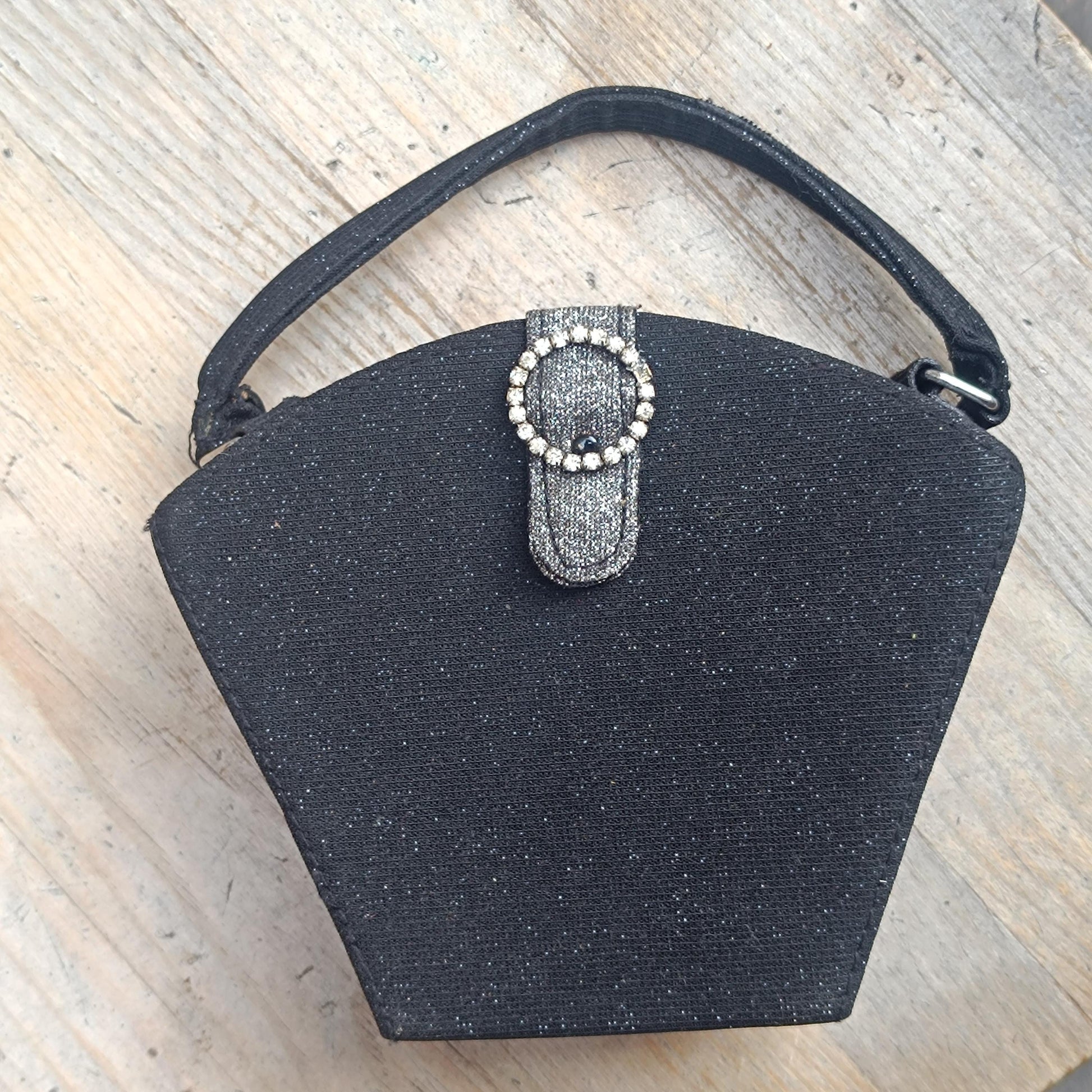 Vintage y2k Black glitter mini bag with top handle and faux-bling detail is laid flat on a wooden surface. The compact design is perfect for raves or an evening out on the town