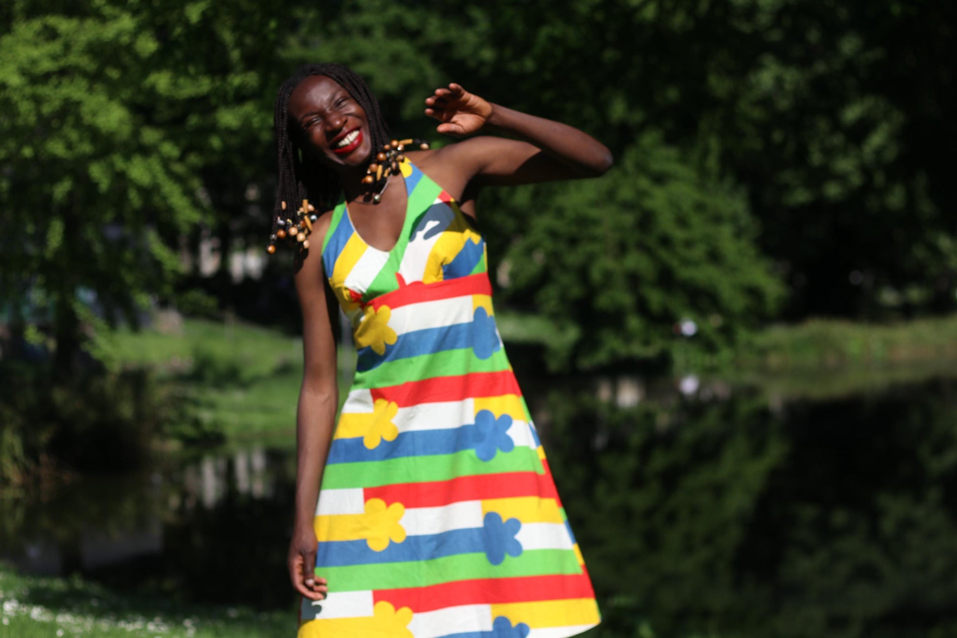 Retro 70s summer halterneck dress in vivid Scandinavian print, worn on. smiling model with beaded braids on a sunny day outdoors&quot;