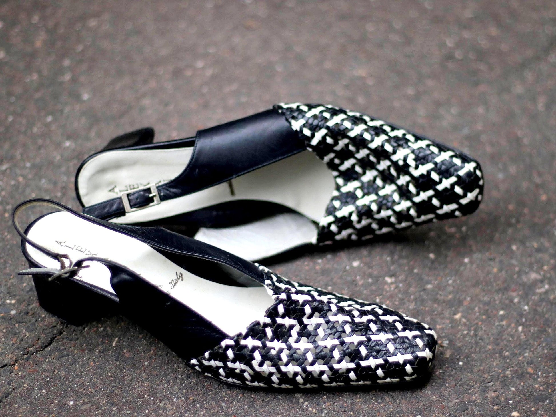 a pair of vintage Alexandria Italian-made woven slingback pumps featuring a black-and-white basket-weave design, pointed toe, and block heel. The 90s design is finished with a sleek leather slingback and an adjustable buckle.