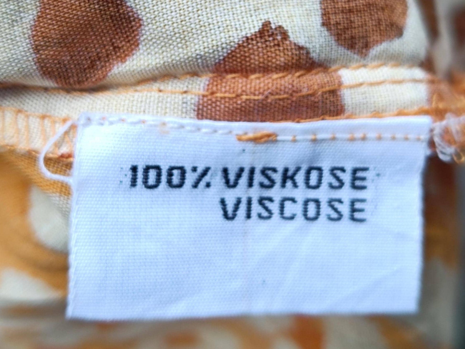 detailed shot of a fabric tag for a vintage 90s animal print blouse in yellow. The tag reads 100% viscose