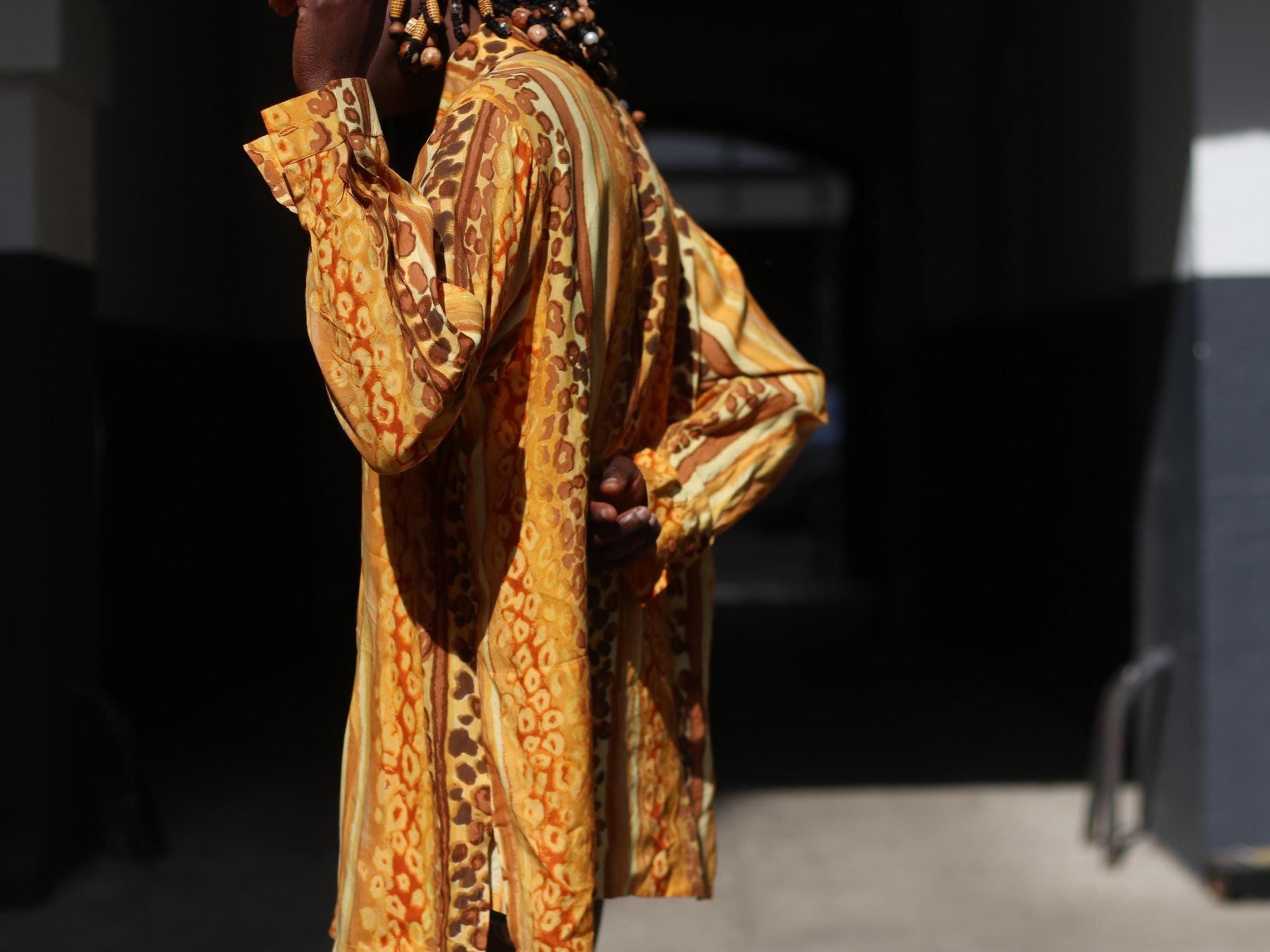A detailed outdoor shot of a person wearing a yellow patterned blouse and blue jeans. The focus is on the animal-print of the 90s blouse and the oversized silhouette