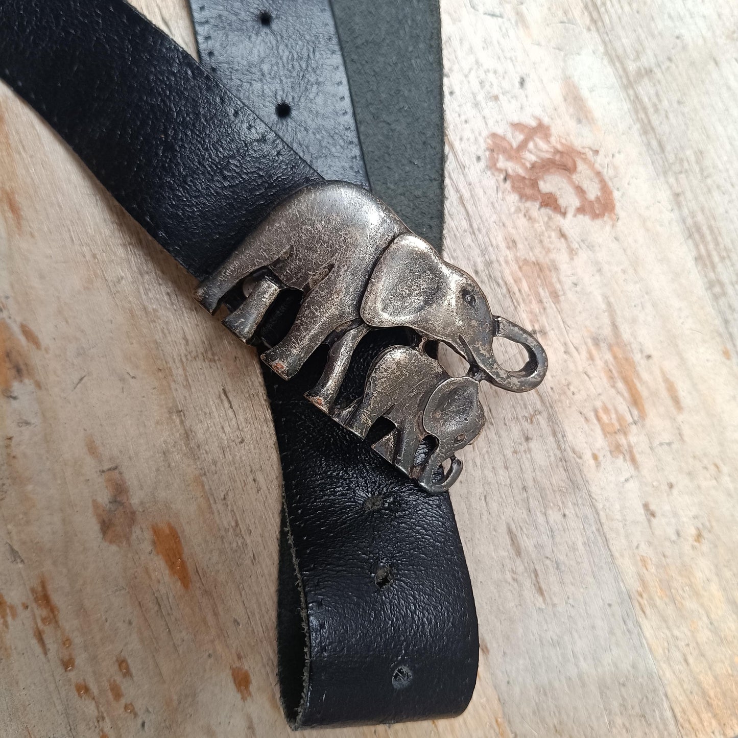 Close-up of a vintage black leather belt with an antique silver elephant buckle, showcasing intricate front detailing. The 70s handmade piece is photographed on a  wooden brown rustic surface